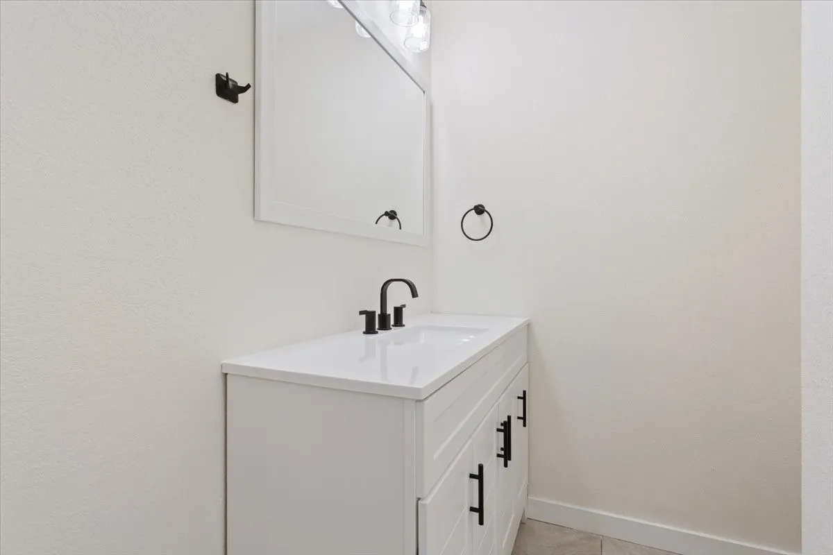 Downstairs bathroom #2, attached to kitchen. White vanity with black hardware and an integrated sink