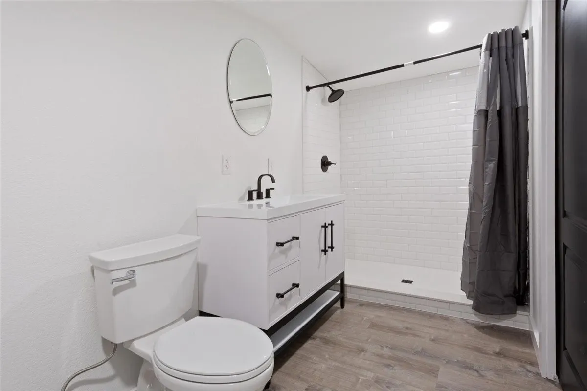 Second primary bathroom (upstairs) #3. Bathroom featuring a white vanity with matte black hardware, white subway tile shower surround, matte black shower fixtures, and wood-finish flooring