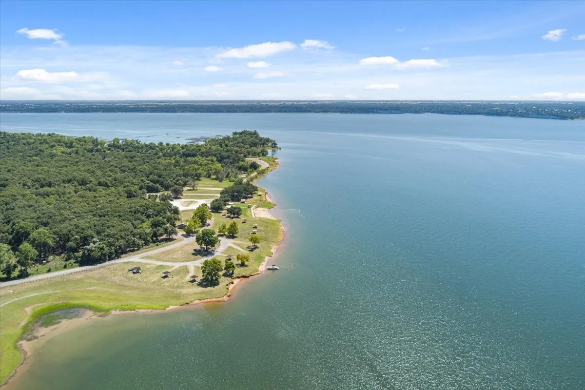 Expansive waterfront image featuring a tree-lined shore, sandy beach areas, and a paved access road