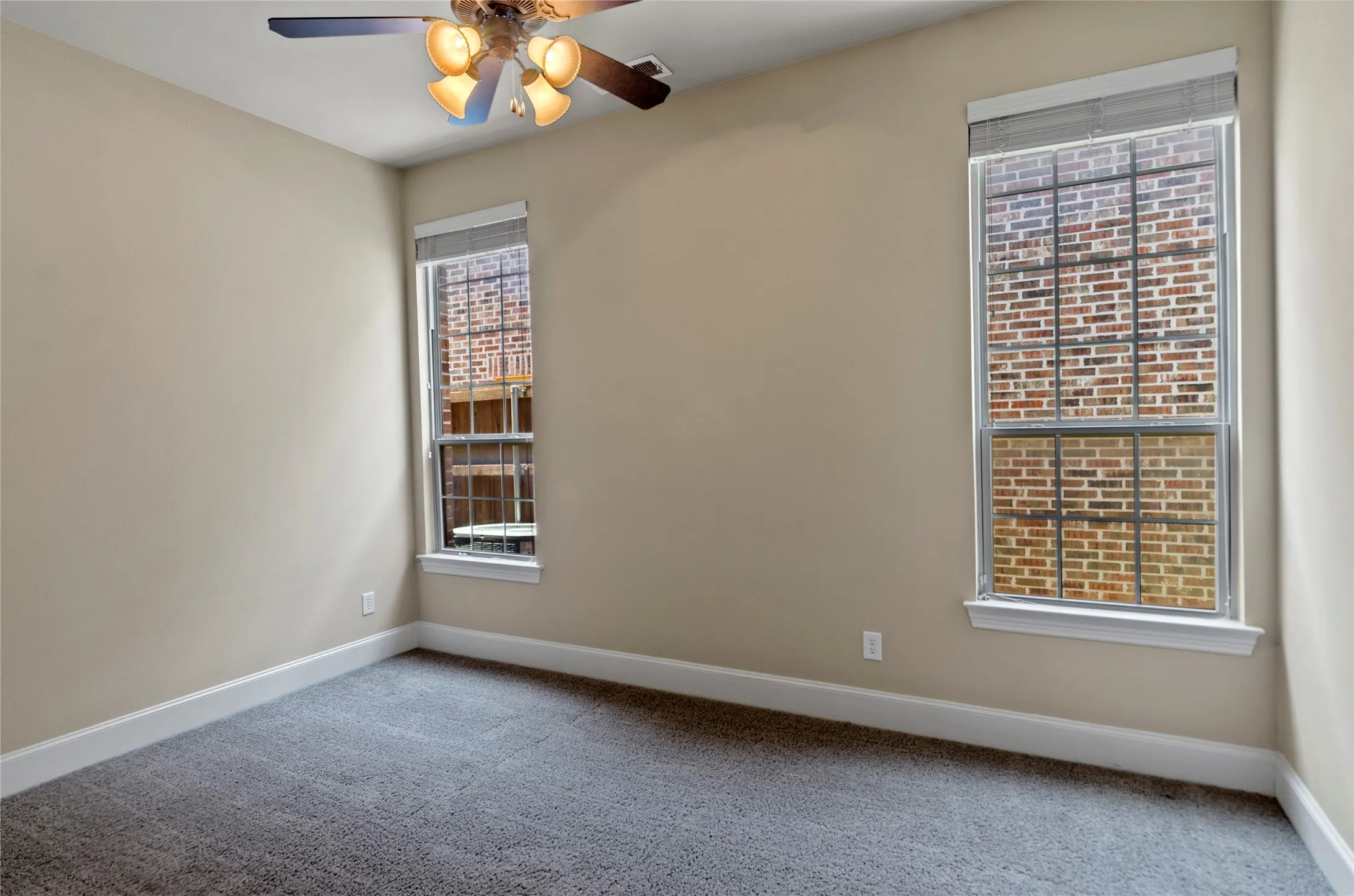 Bedroom featuring light neutral walls, gray carpet, white baseboards, and two double-hung windows with blinds