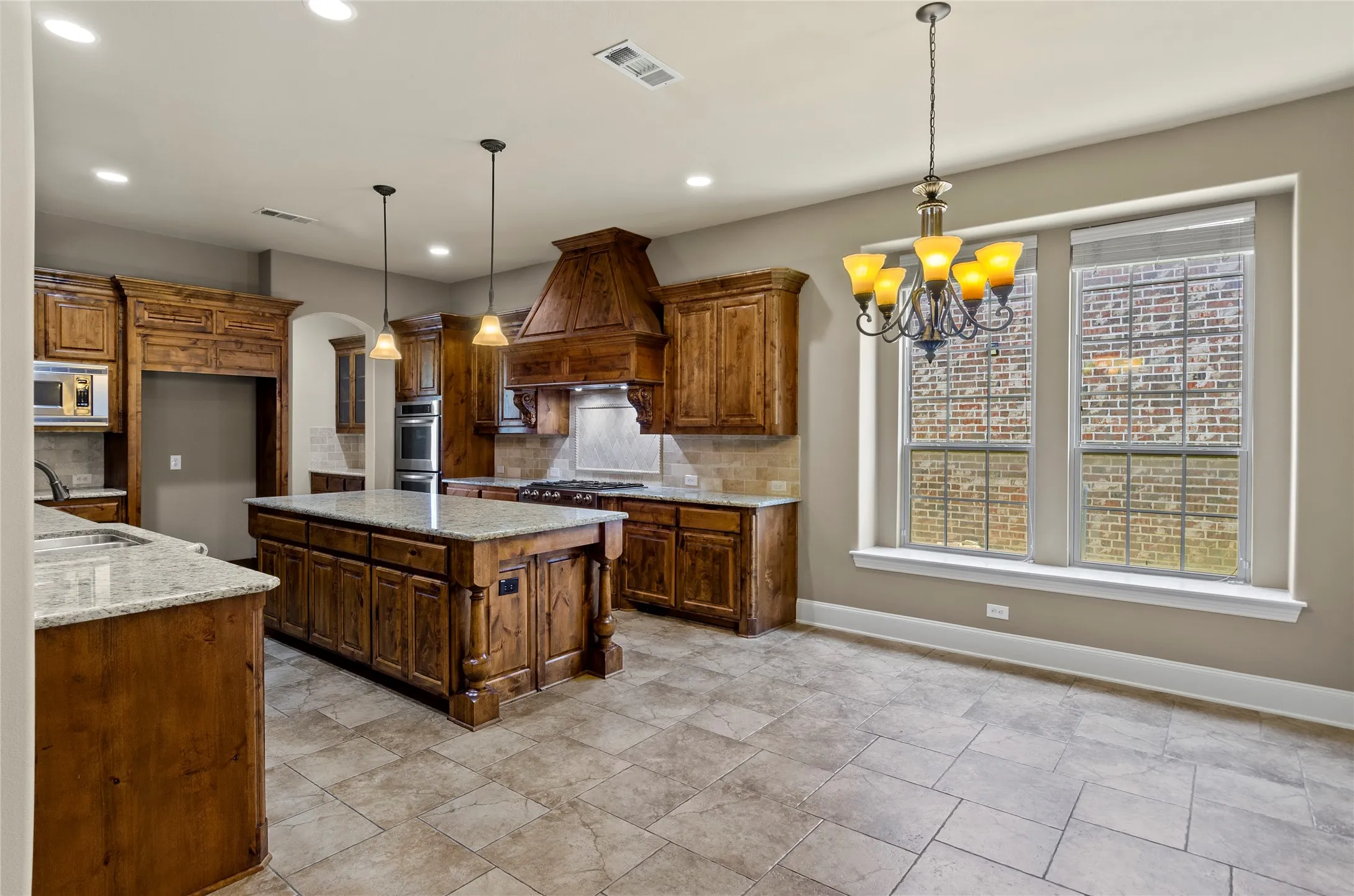 Spacious kitchen featuring an oversized island with granite countertop, abundant wood cabinetry, tile flooring, and a built-in oven