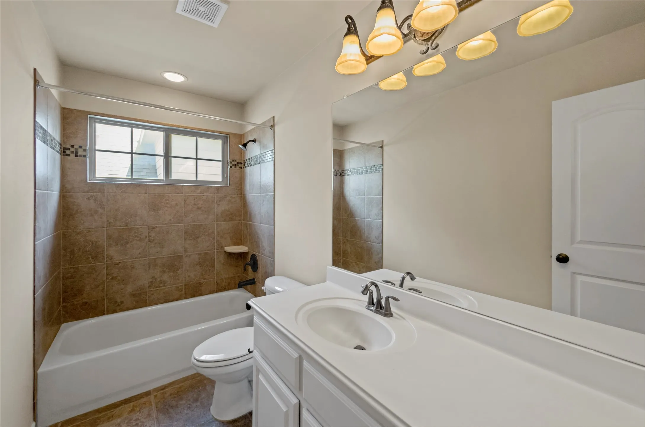 Bathroom featuring a combination shower and tub with brown tile surround and decorative accent band