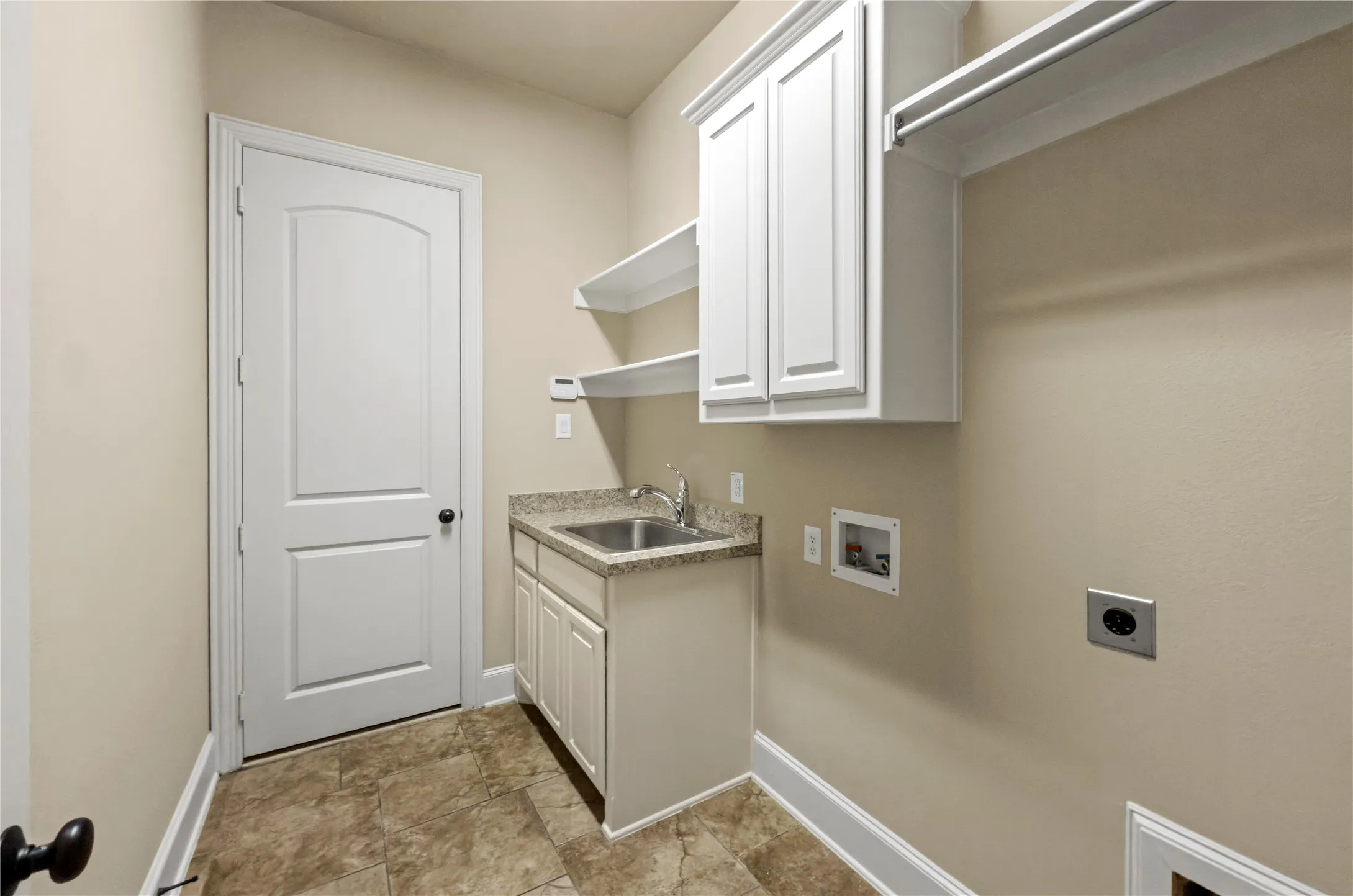 Utility room featuring tile flooring, white cabinetry, a sink with a granite-look countertop, and open shelving