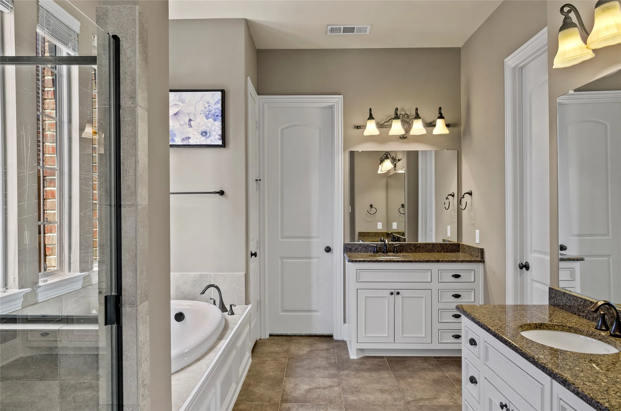 Bathroom featuring dual vanities with granite countertops, integrated sinks, and dark bronze fixtures