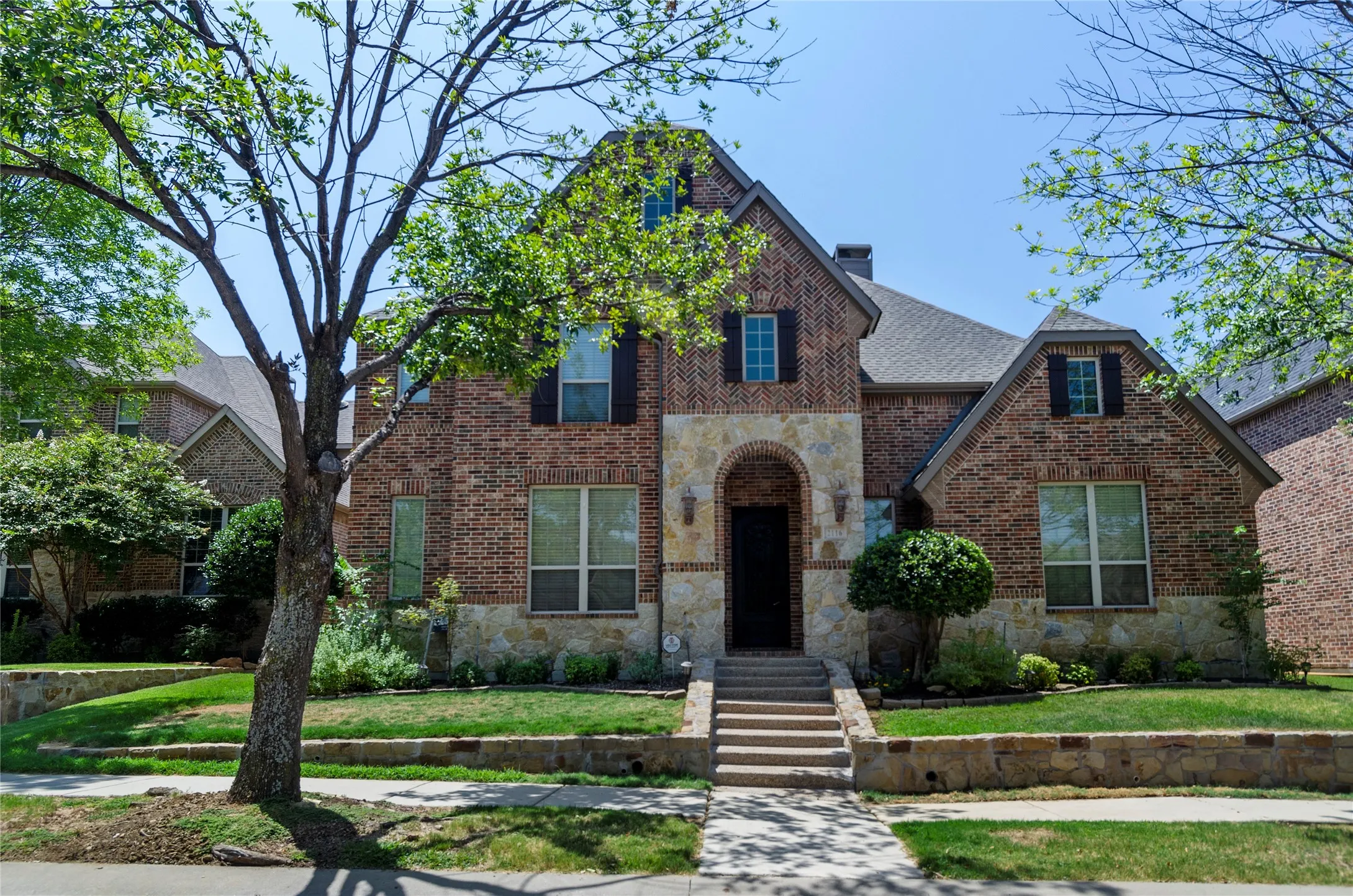 Brick and stone facade residence featuring a prominent arched entry, multiple gables, and dark window shutters