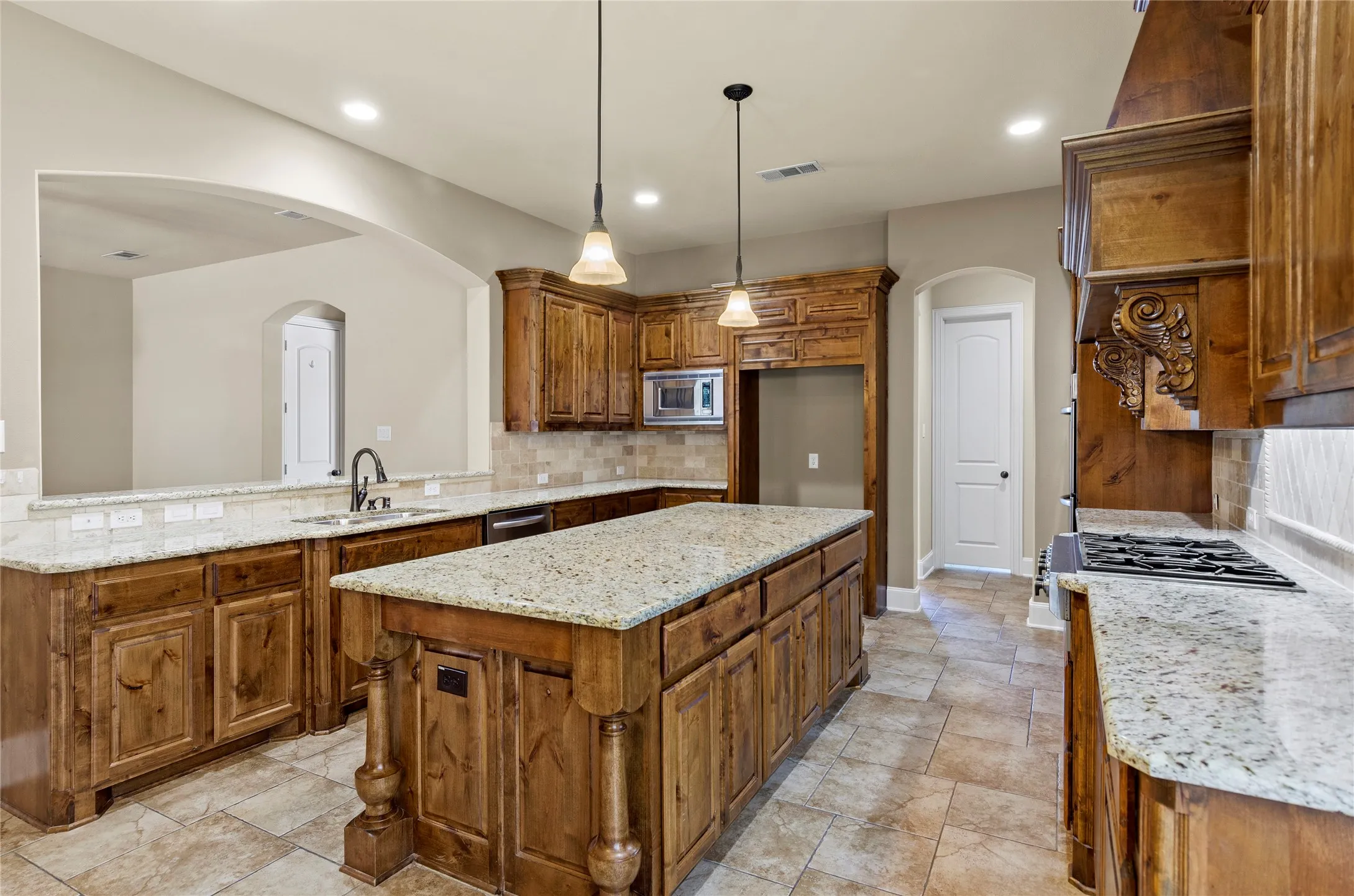 Spacious kitchen featuring an expansive center island, warm wood cabinetry, light granite countertops, tile flooring, and a gas cooktop