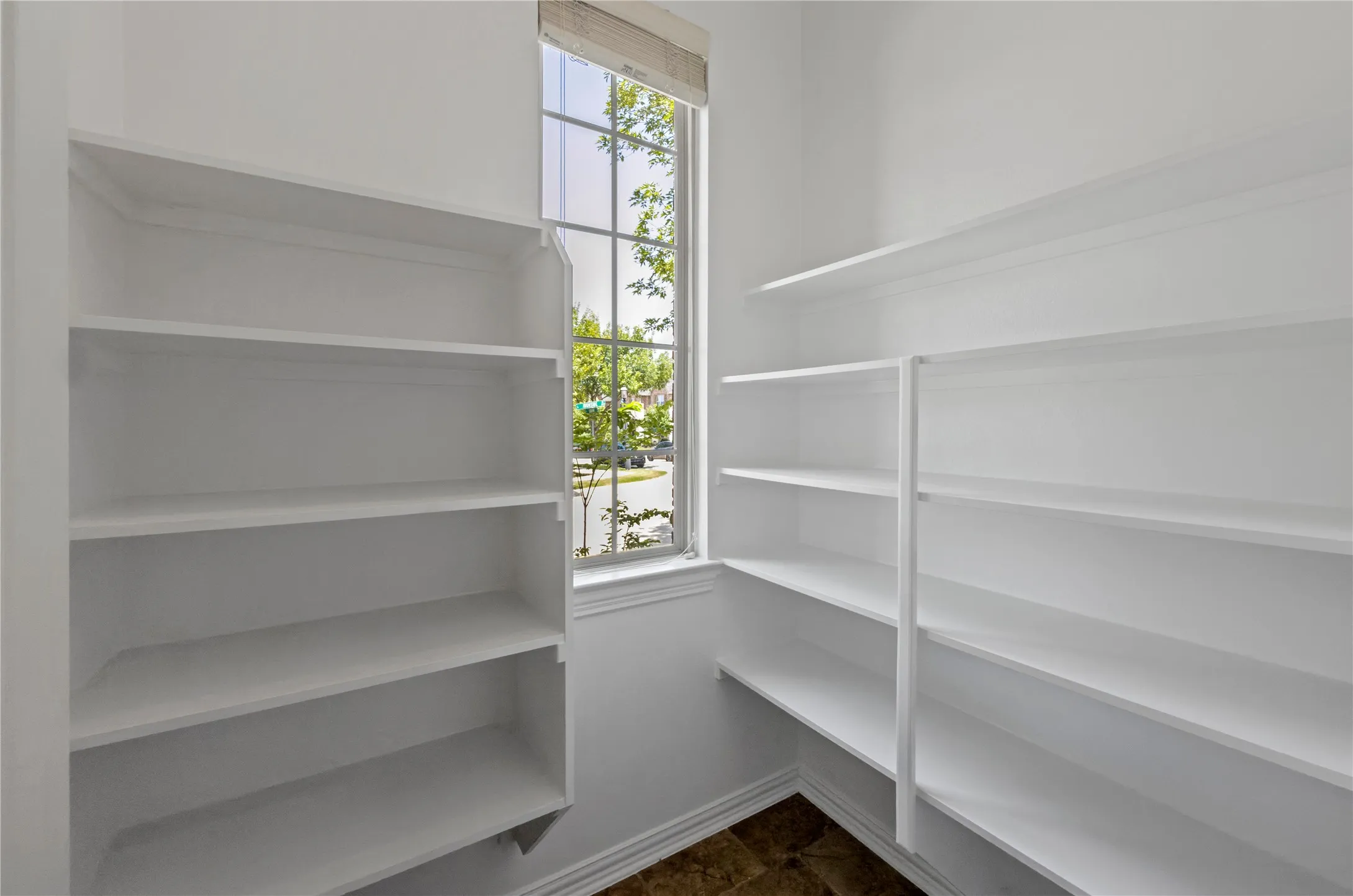 Expansive pantry featuring extensive white shelving, a window with exterior visibility, and patterned flooring