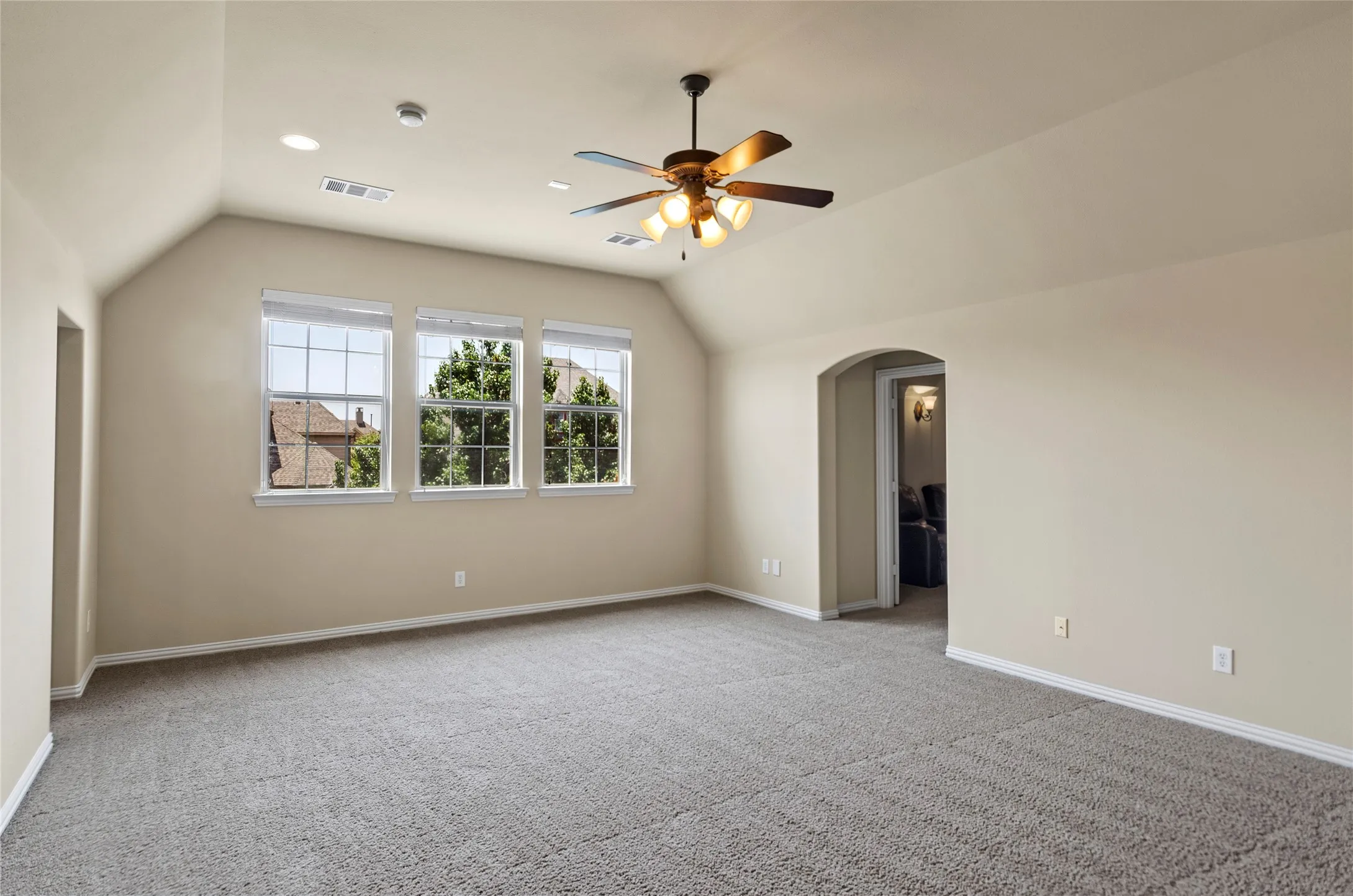 Spacious room featuring vaulted ceilings, recessed lighting, a ceiling fan, three windows, and an arched doorway