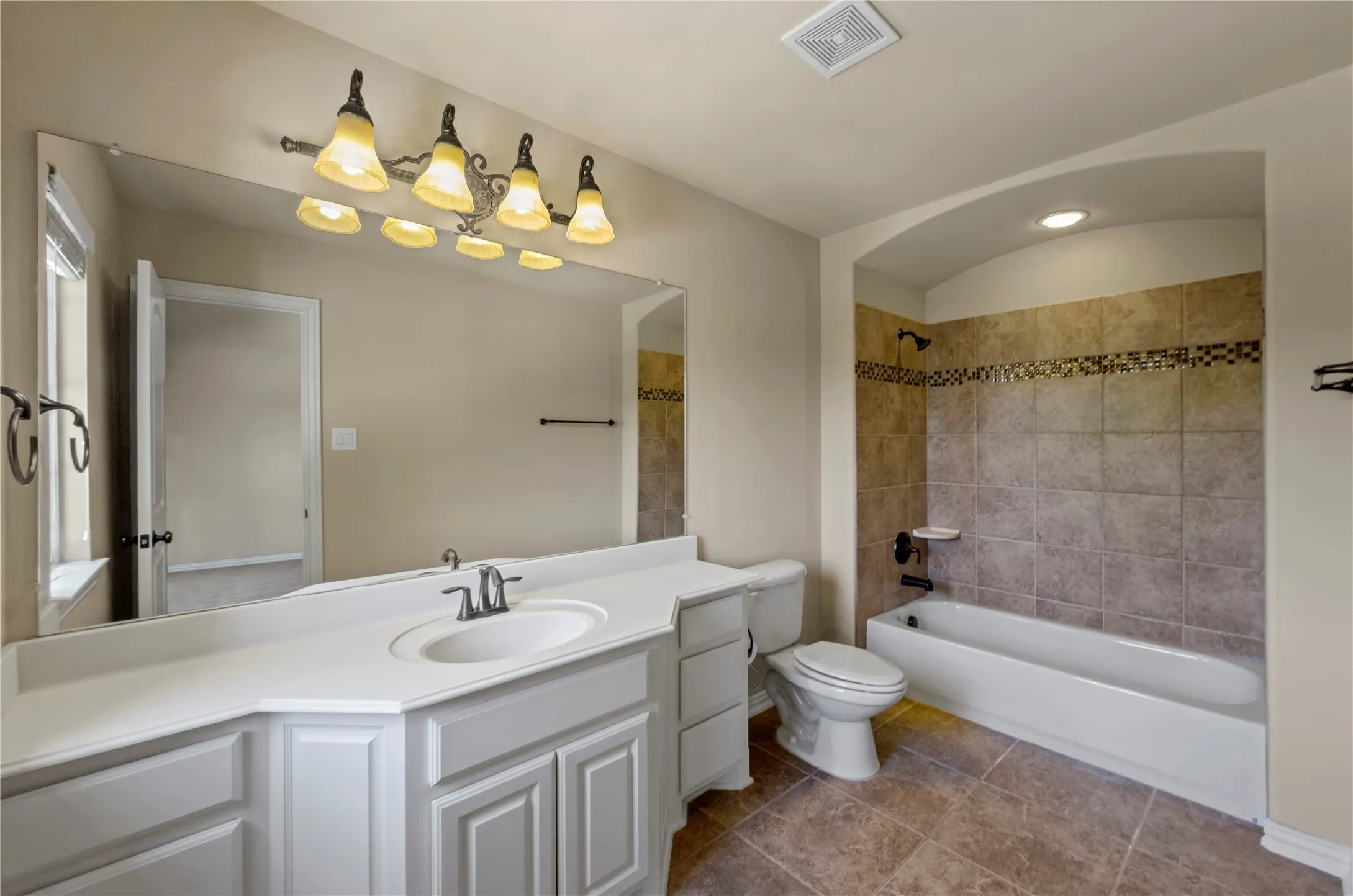 Bathroom featuring a white vanity with an integrated sink and chrome faucet, a large wall-mounted mirror, and an arched alcove with a tiled tub/shower combination