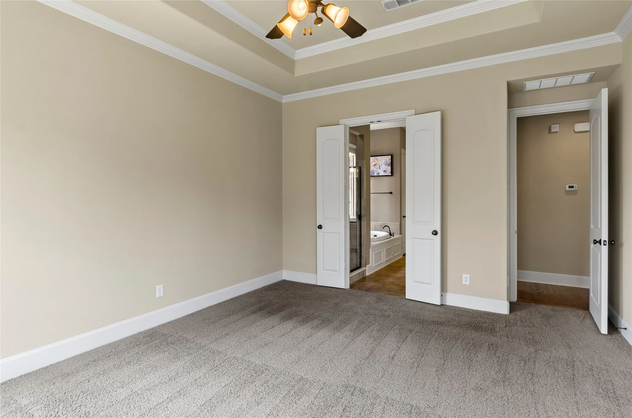 Tray ceiling with crown molding, ceiling fan, neutral wall color, carpeted flooring, and a double-door entryway