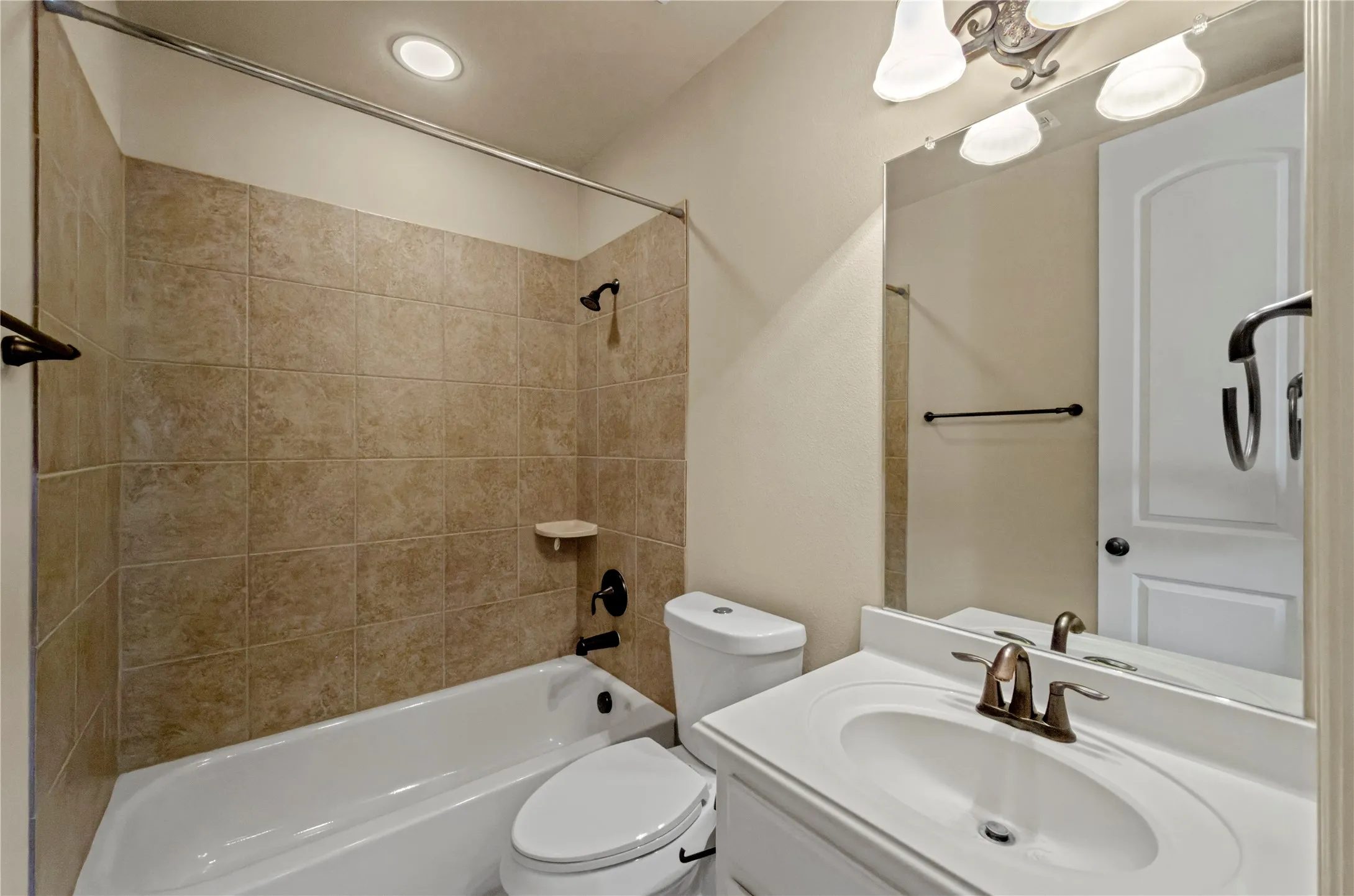 Full bathroom featuring a white bathtub and commode, tiled shower surround, recessed ceiling lighting, and a vanity with a white countertop and integrated sink