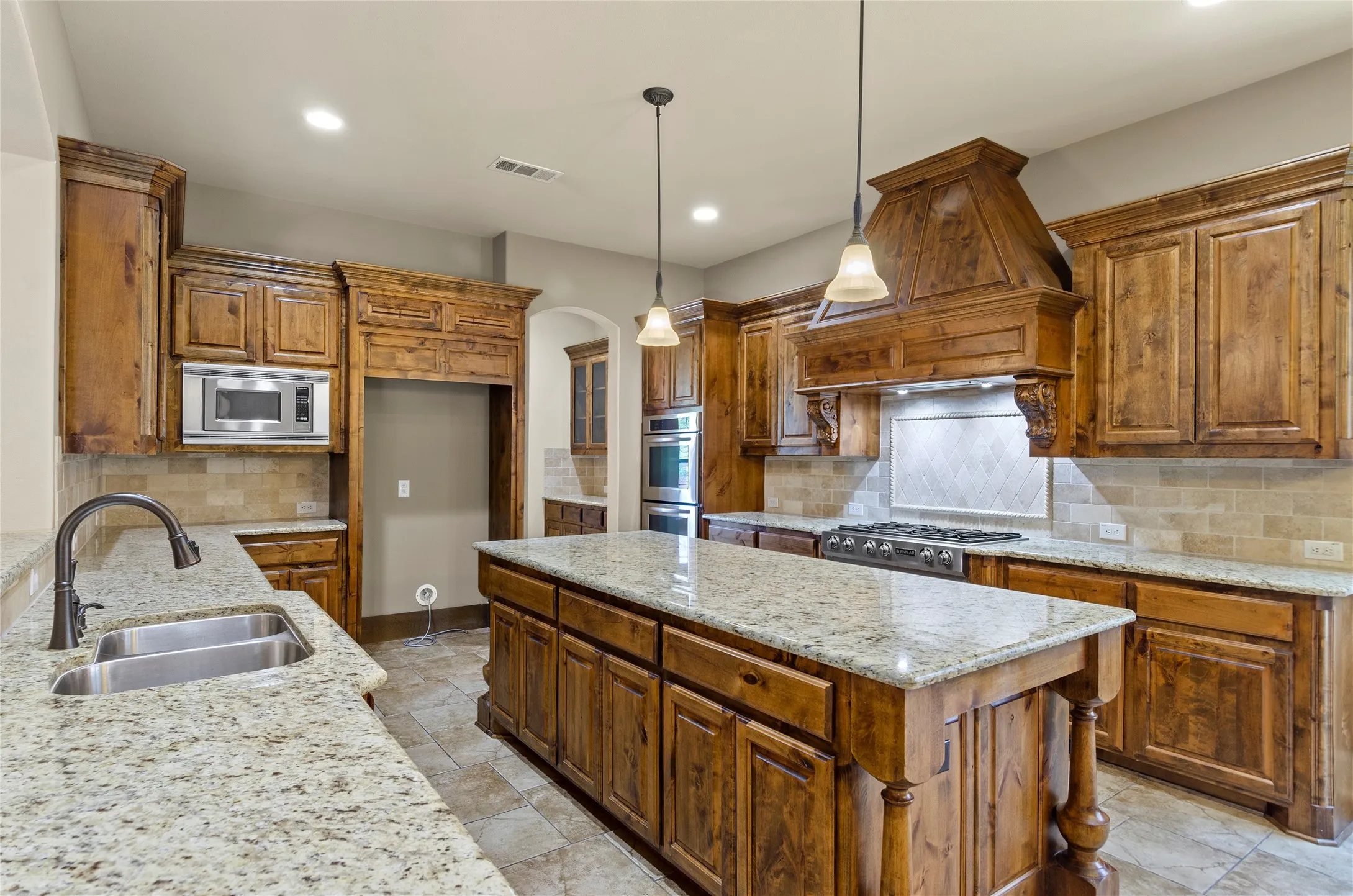 Expansive kitchen featuring a large central island, granite countertops, wood cabinetry, stainless steel appliances, and tile flooring
