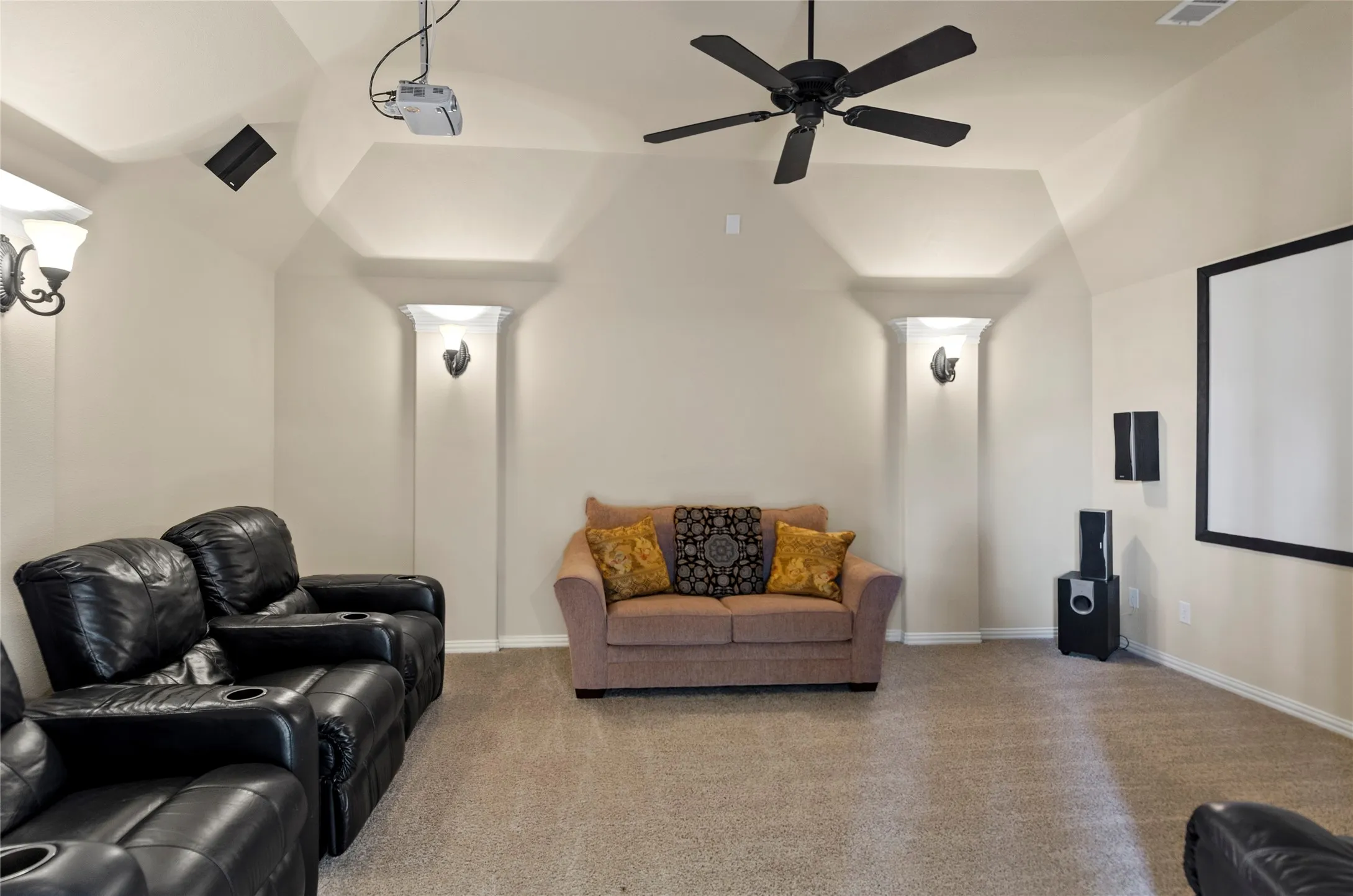 Dedicated media room featuring a mounted projector, ceiling fan, and carpeted flooring