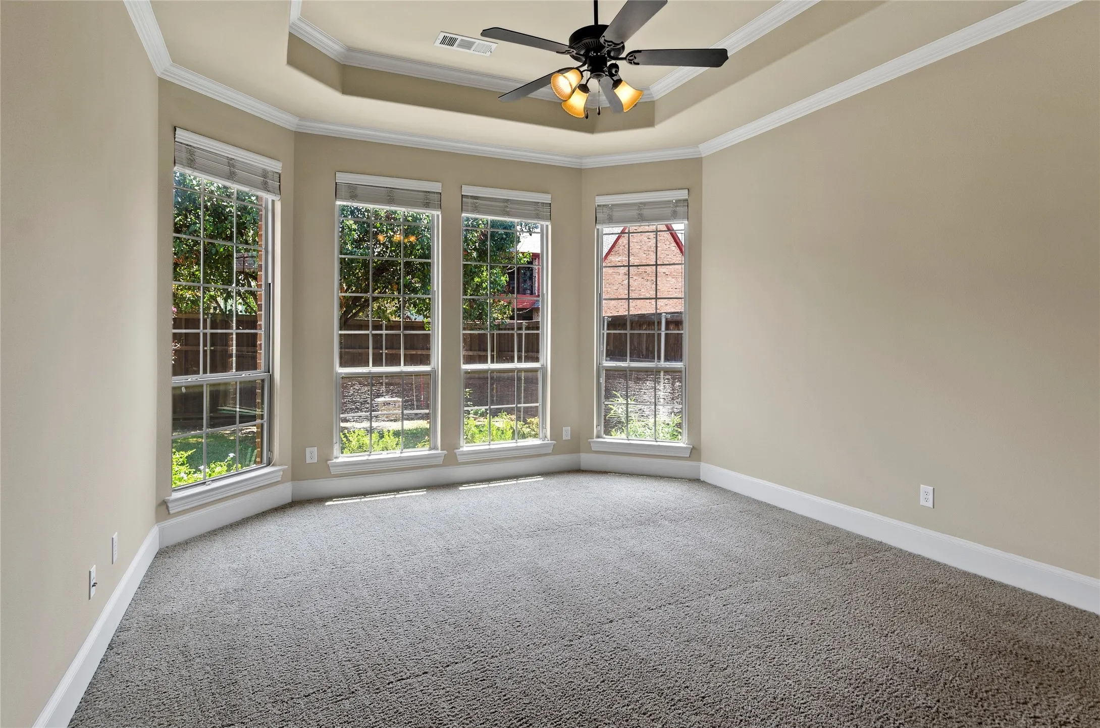 Spacious room with a bay window design, tray ceiling, and a ceiling fan