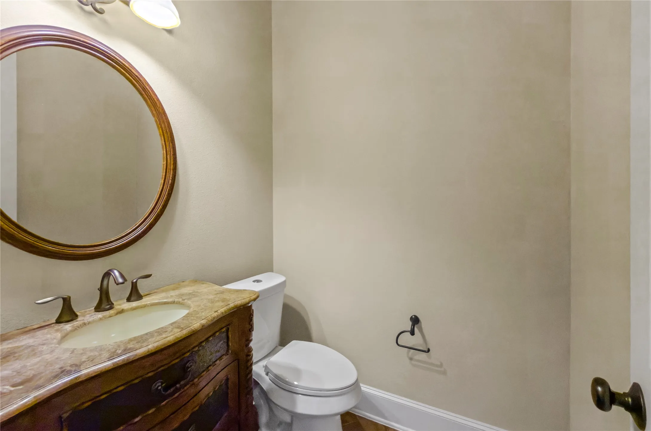 Powder room featuring a decorative wood vanity with integrated sink, stone countertop, a round framed mirror, and a wall-mounted light fixture