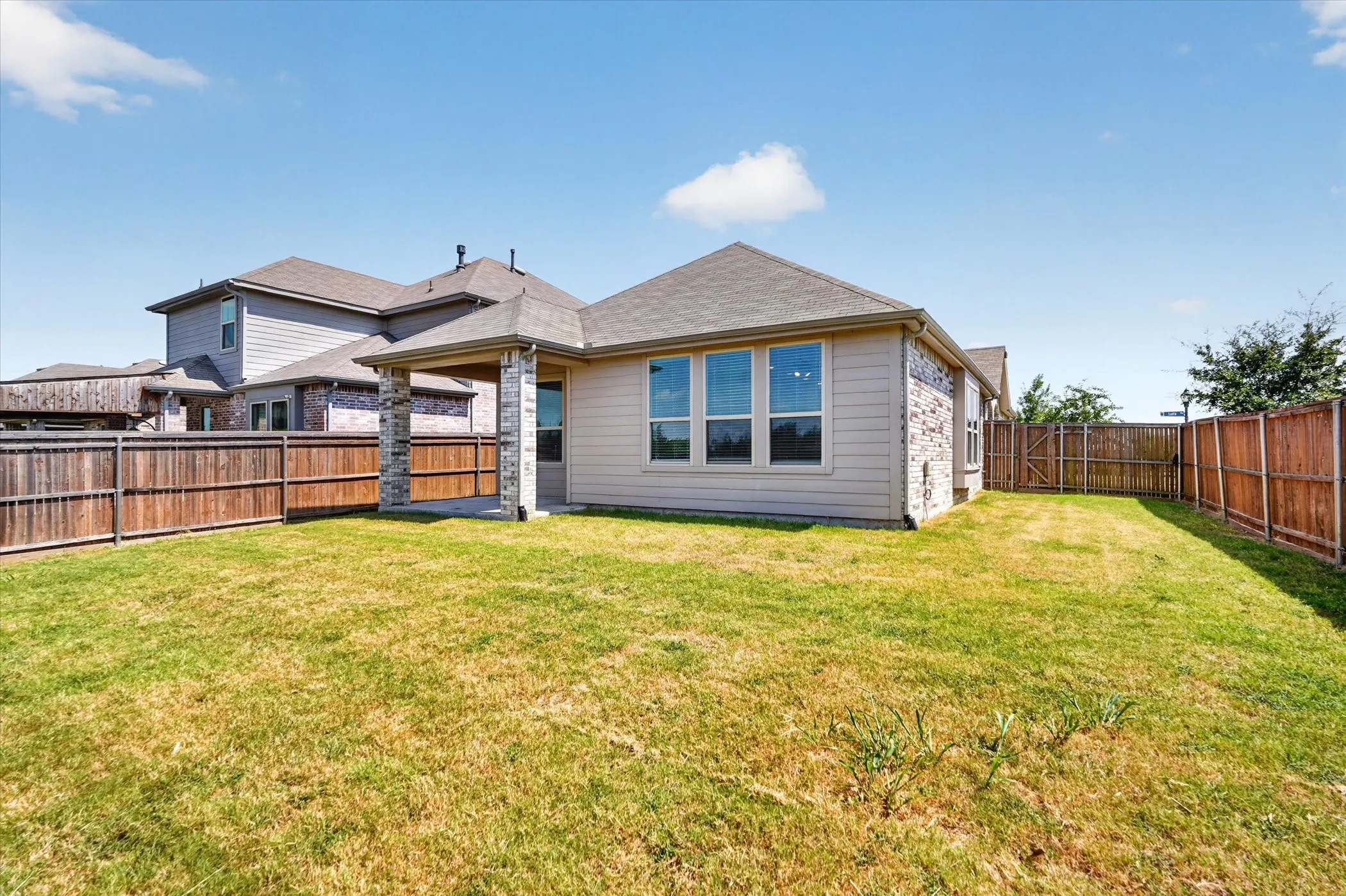 Expansive backyard featuring a covered patio with stone columns, a wood privacy fence, and multiple windows across the rear elevation