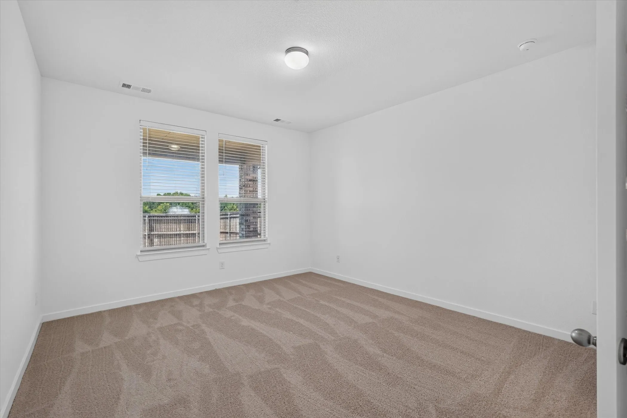 Bright bedroom featuring dual windows with natural light, neutral wall finishes, and wood-finish flooring throughout
