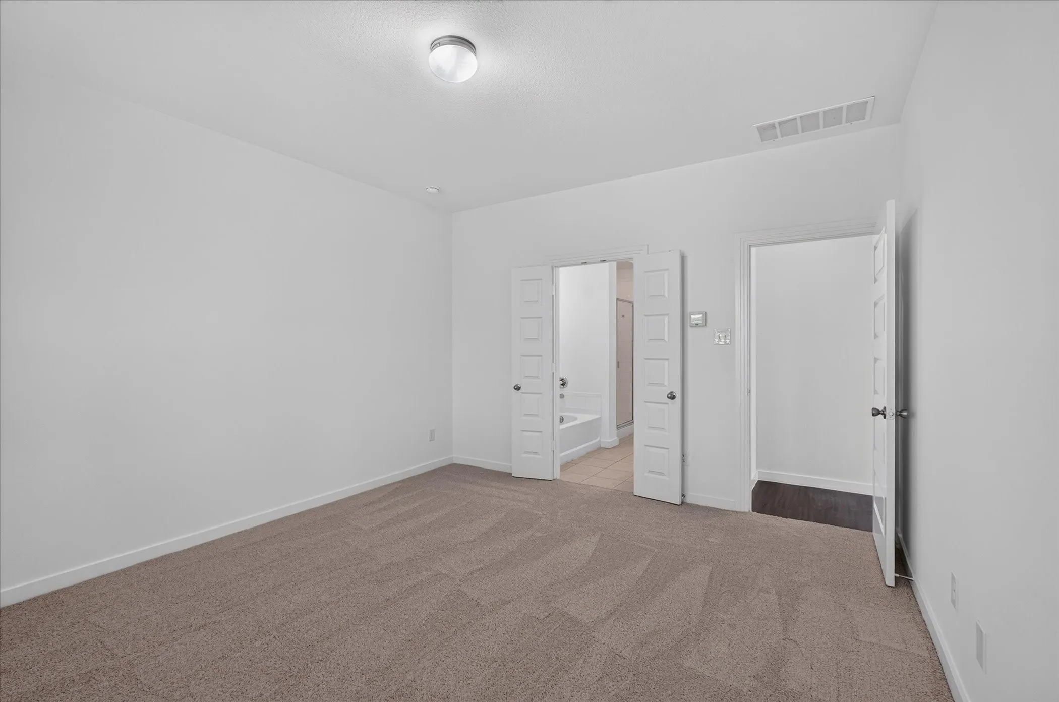 Spacious interior room featuring neutral-toned carpet flooring and a simple flush-mount ceiling light fixture