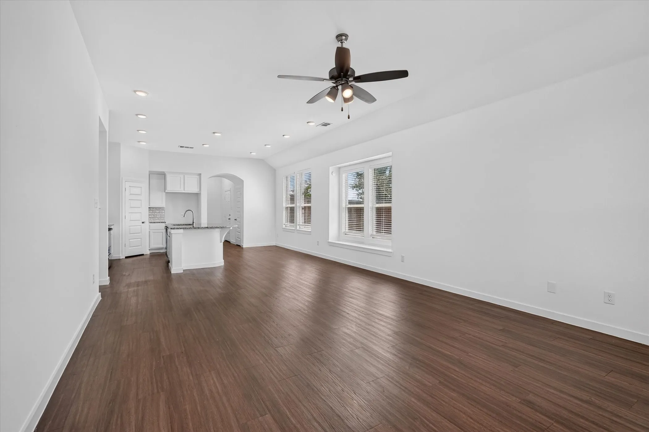 Spacious open-concept living area featuring rich wood-finish flooring throughout, white walls, and abundant natural light from multiple glass doors and windows