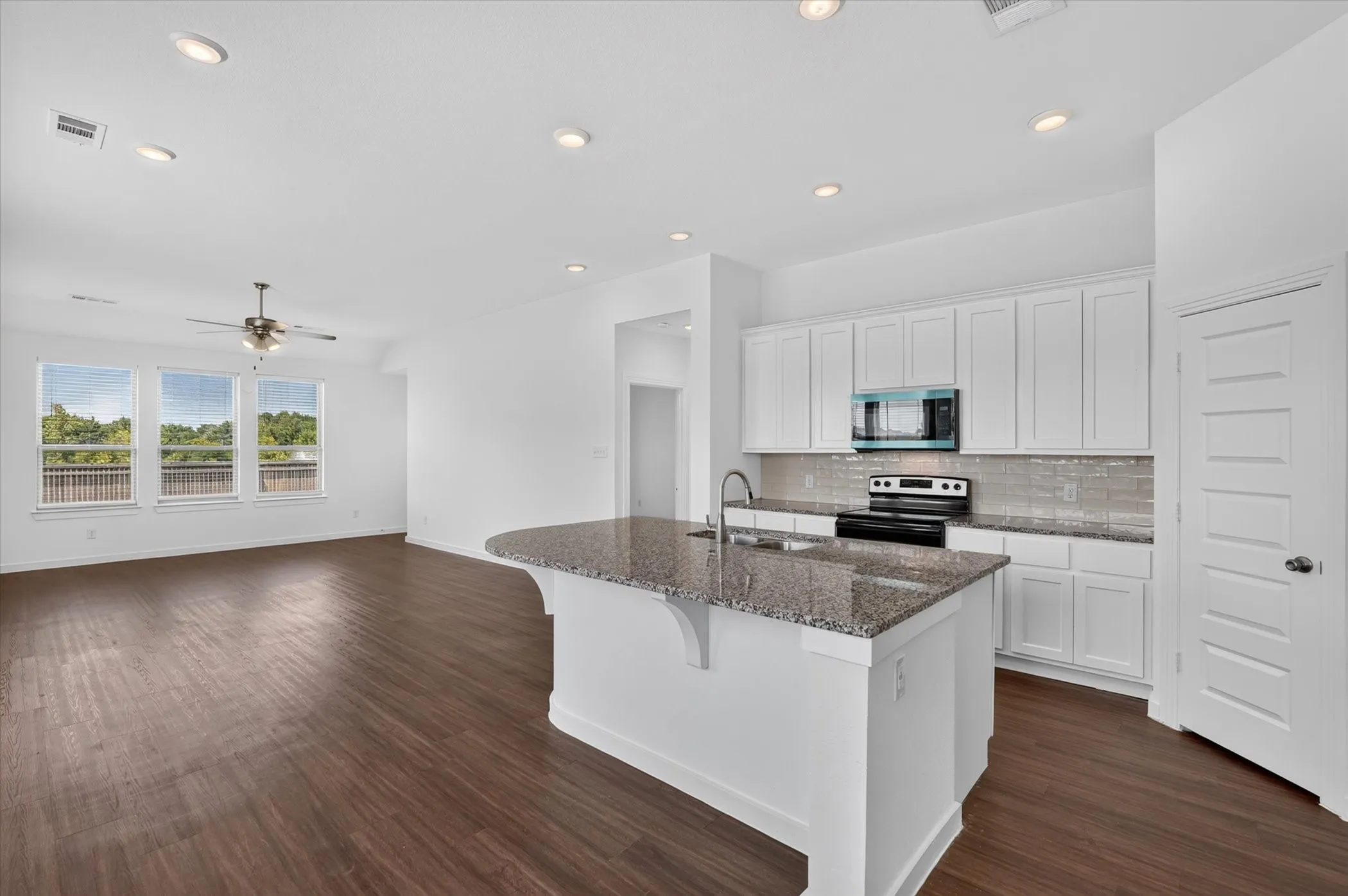 Open-concept kitchen and living area featuring a large island with granite countertop, stainless steel appliances, white cabinetry, and recessed lighting throughout