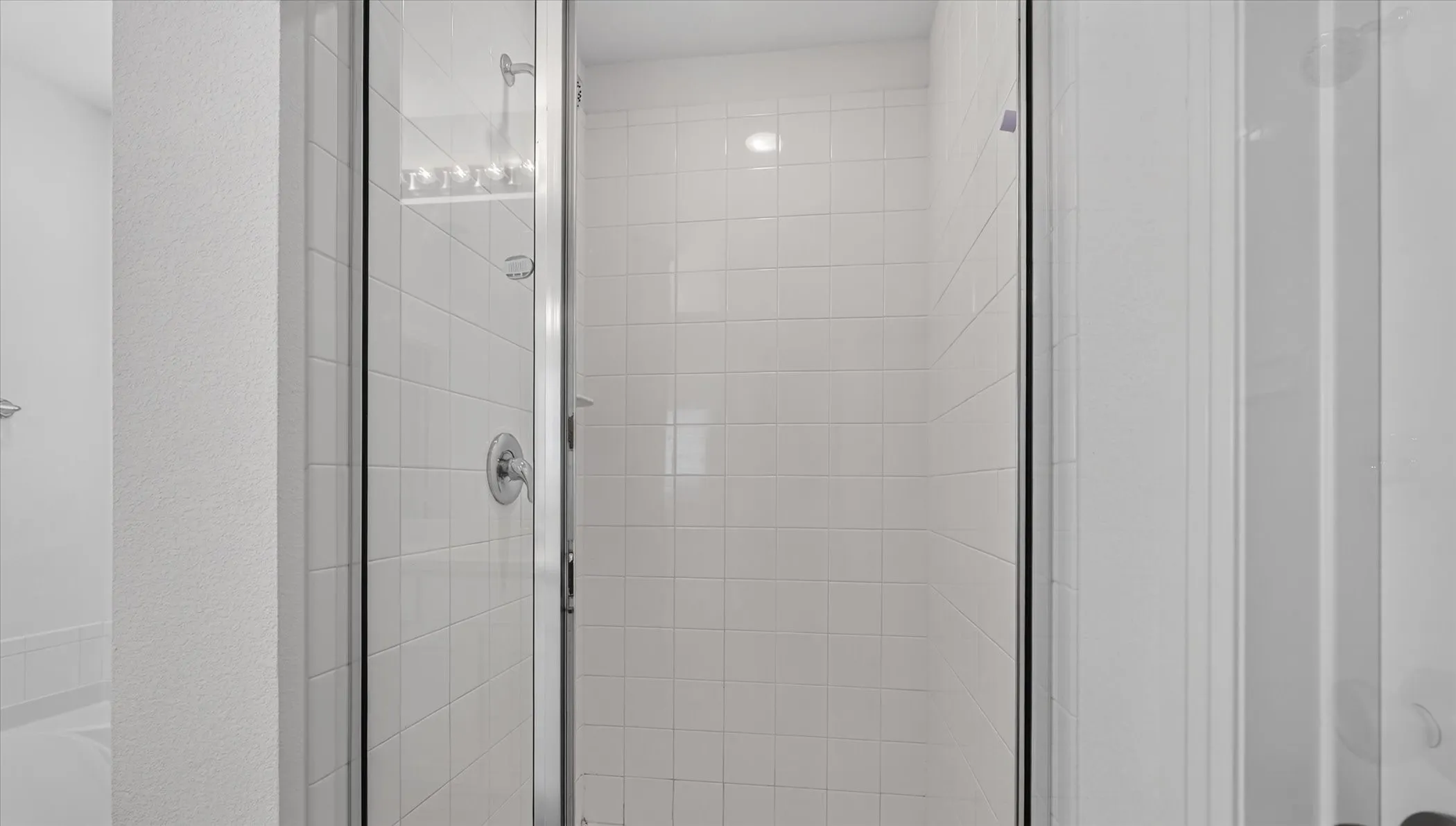 Spa-inspired shower enclosure featuring frameless glass doors, polished chrome hardware, and crisp white subway tile walls with integrated shelving for bath essentials