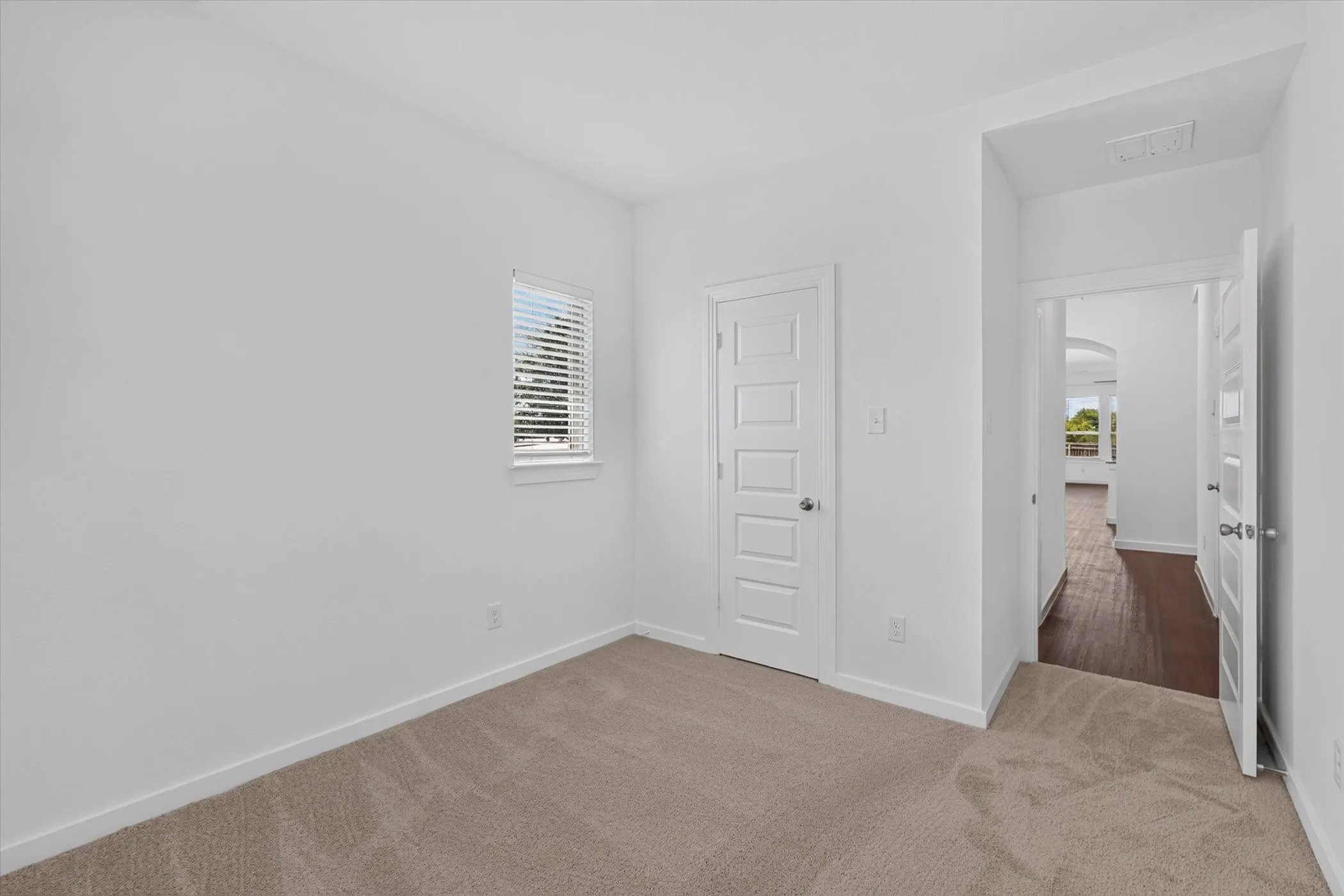 Bright bedroom featuring neutral carpeting, white six-panel interior doors, and a small fixed window with plantation shutters