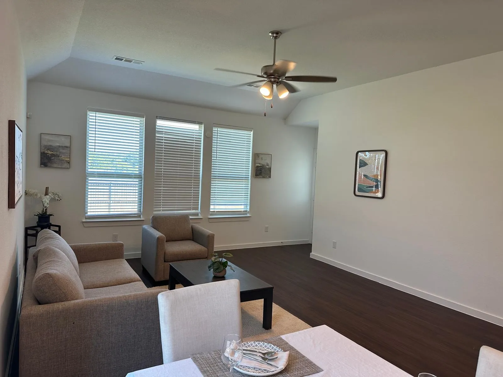Vaulted ceiling with a ceiling fan, three windows with blinds, and wood-finish flooring