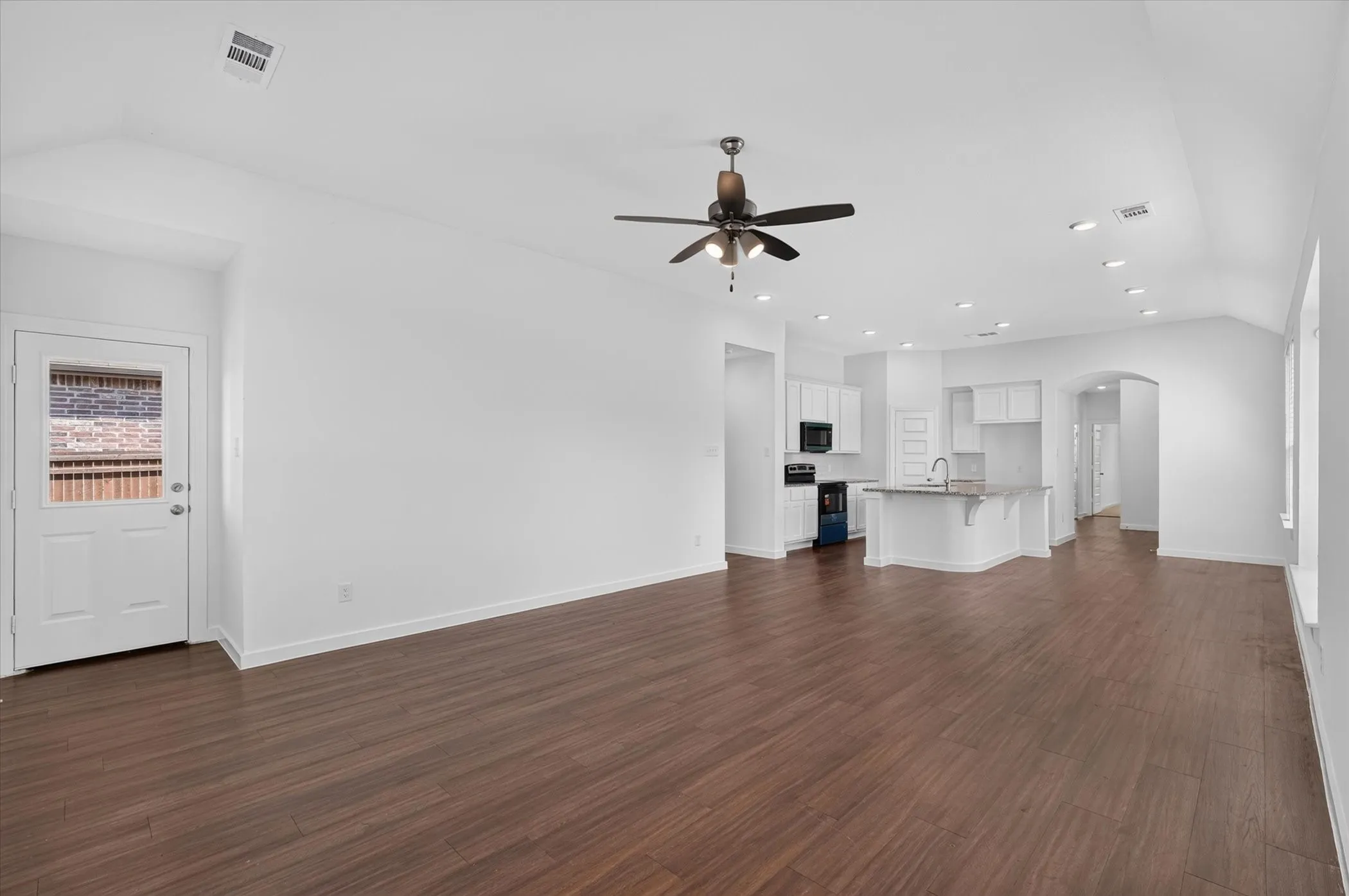 Expansive open-concept living area featuring wood-finish flooring, vaulted ceilings, and recessed lighting
