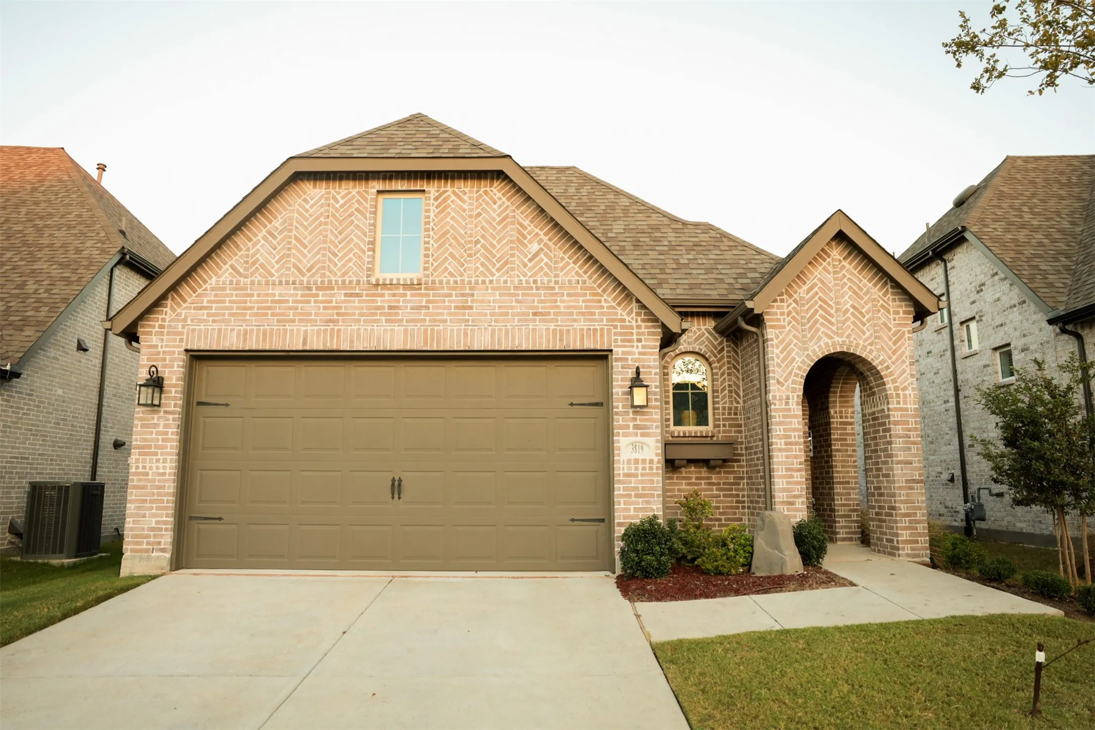Brick facade featuring an arched entryway and a two-car garage