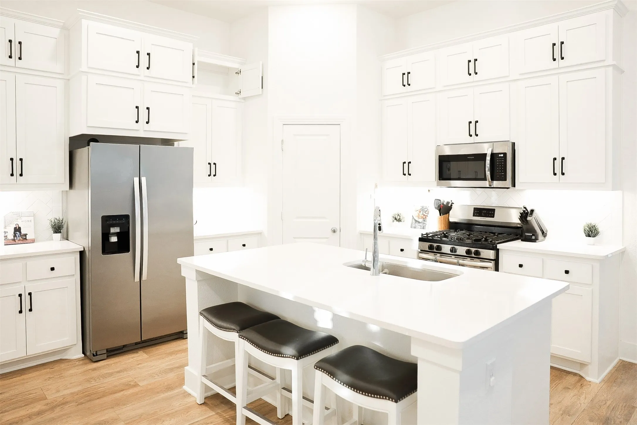 Kitchen featuring white cabinetry with black hardware, stainless steel appliances, a center island with a sink, and wood-finish flooring