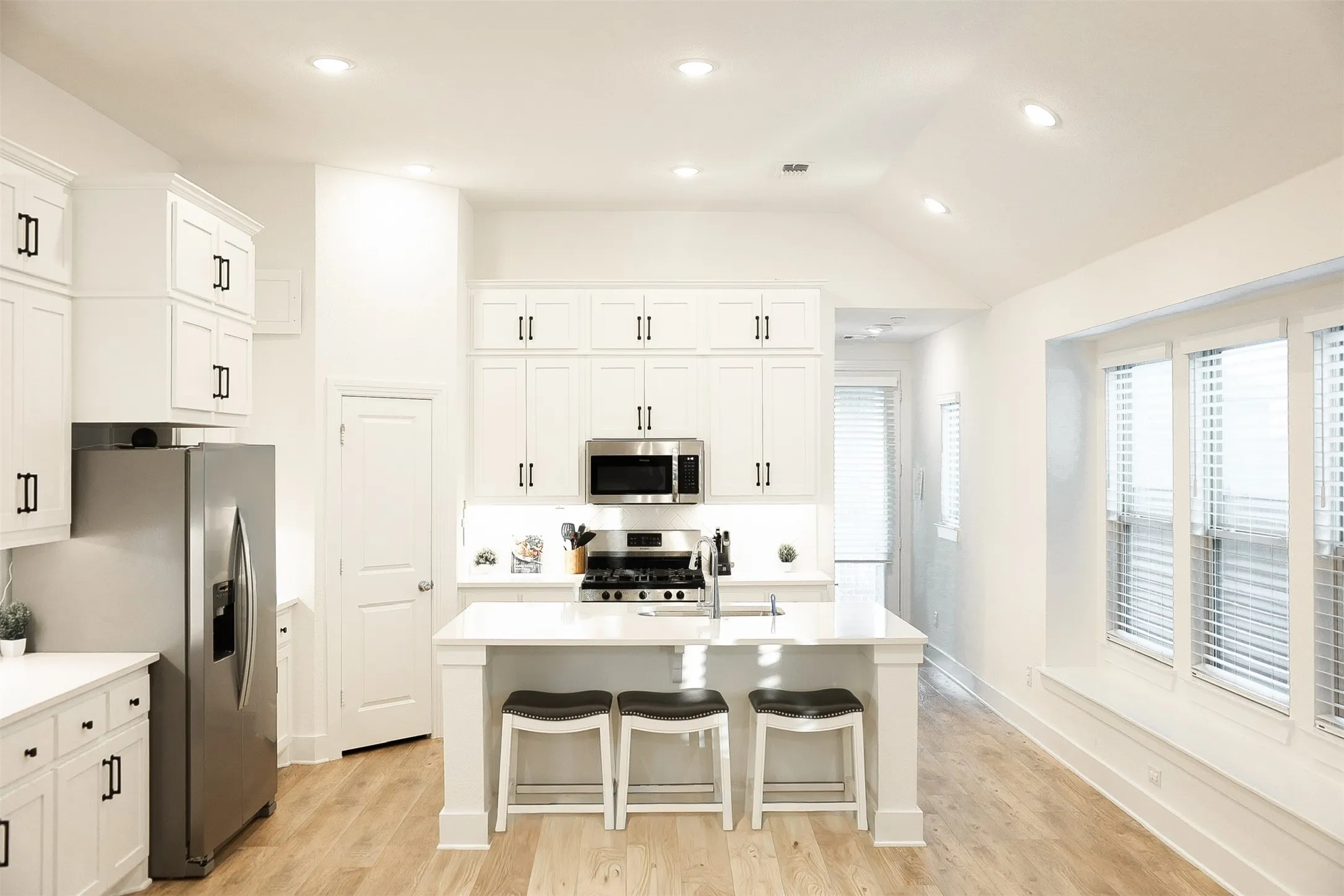 Modern kitchen featuring white shaker cabinetry, stainless steel appliances, a center island with seating, and wood-finish flooring