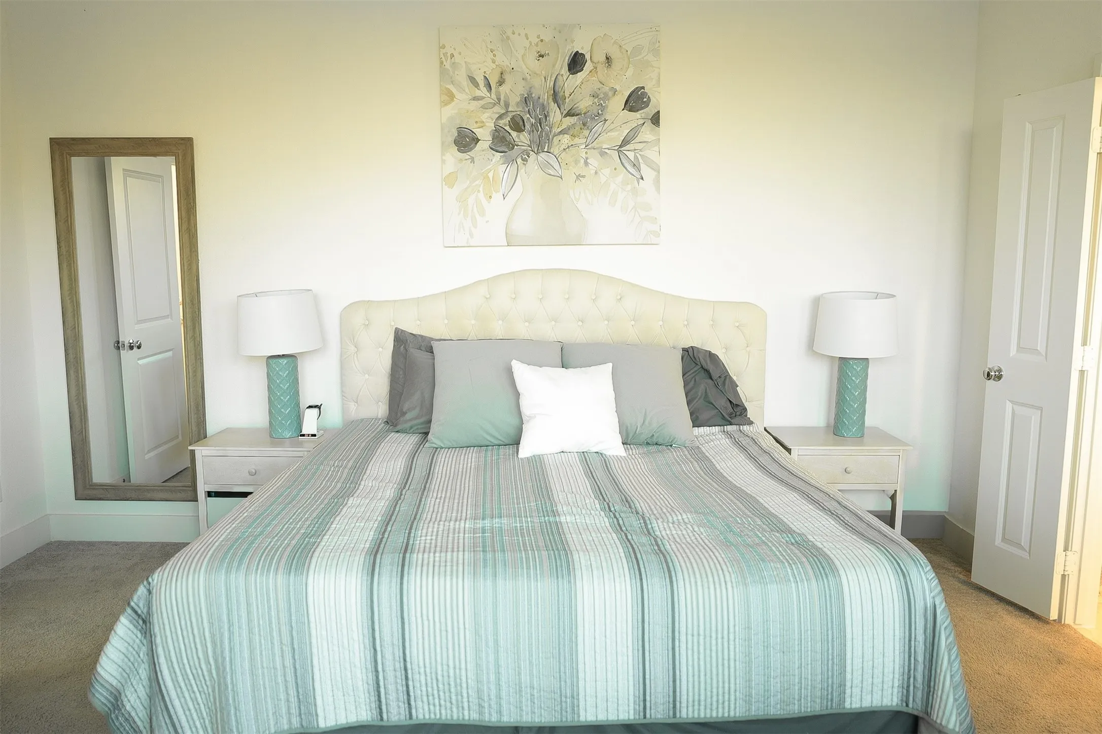 Bright bedroom with carpeted flooring, white walls, a tufted headboard, and two white panel doors