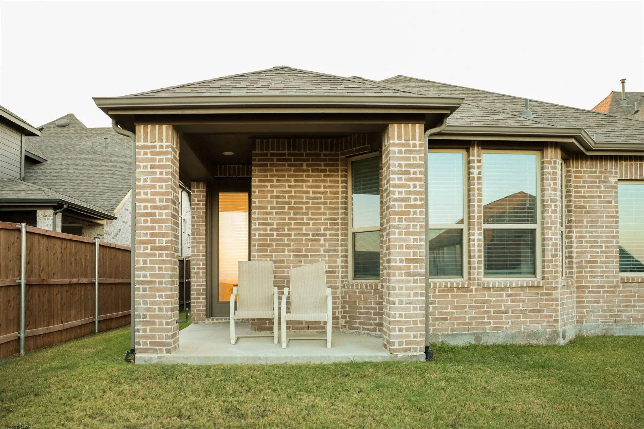 Brick exterior featuring a covered patio with concrete flooring, multiple windows with blinds, and a shingled roof