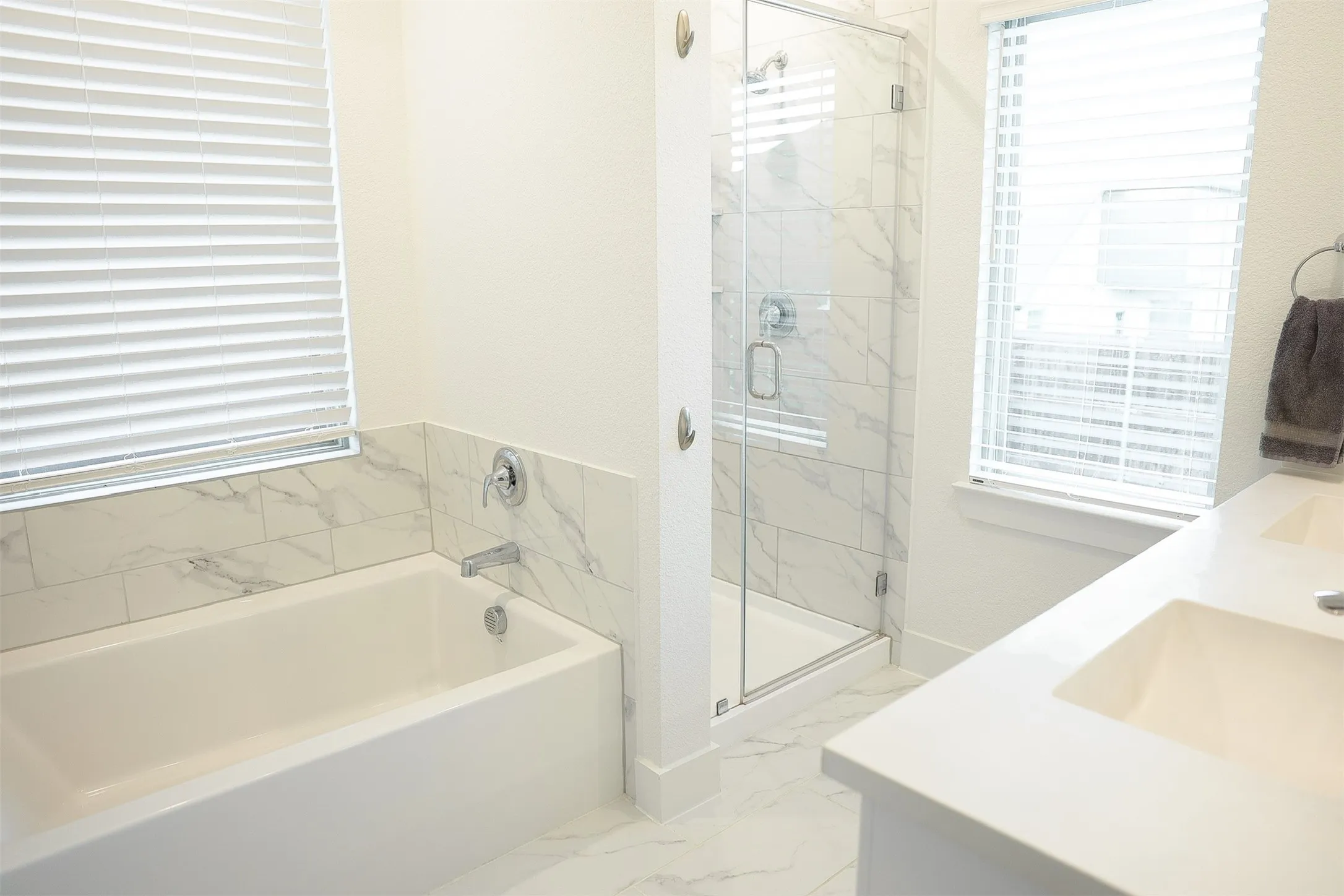 Bathroom featuring a built-in tub with tile surround, a glass-enclosed shower with tile walls, and a dual-sink vanity with a solid white countertop
