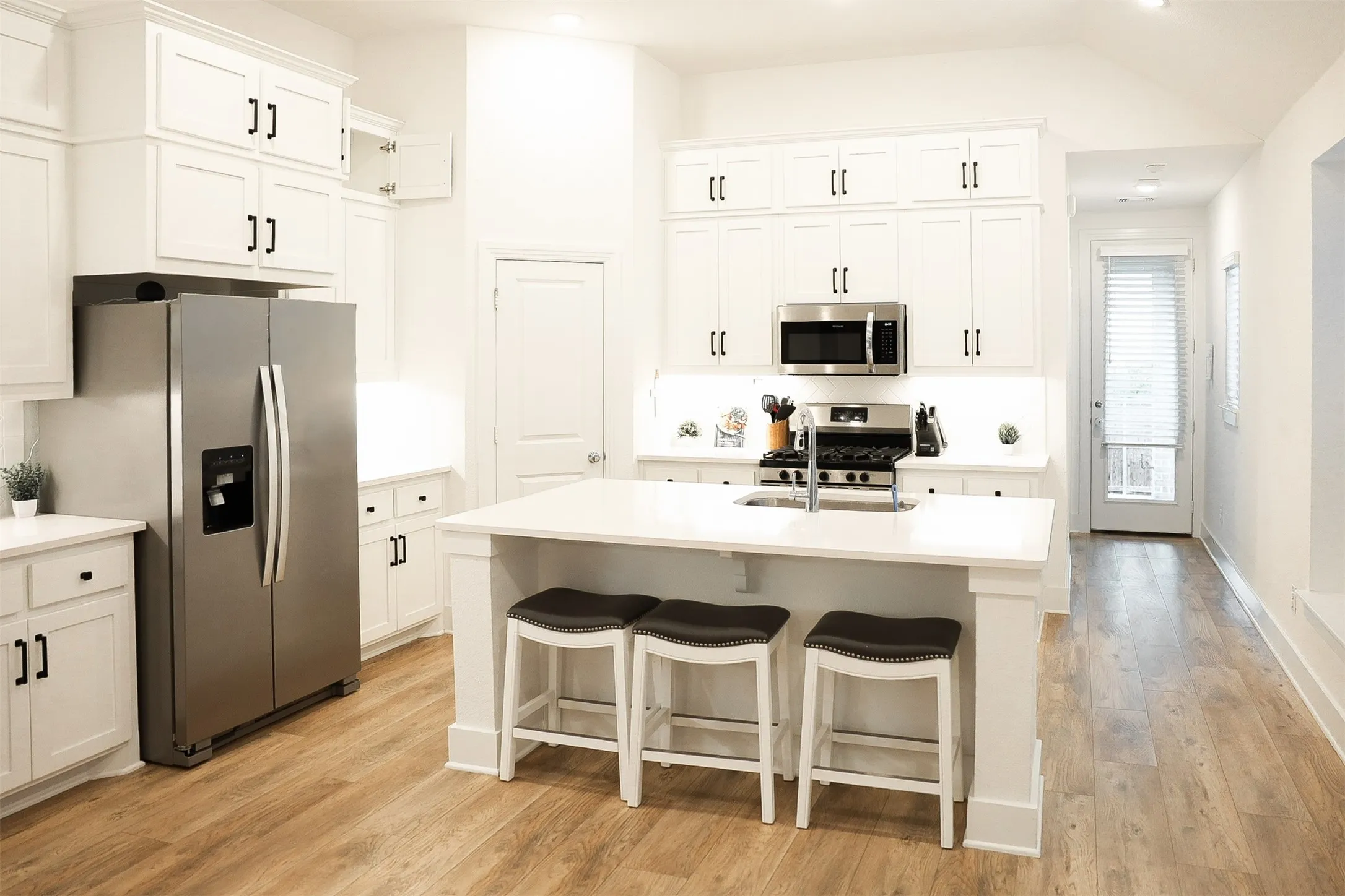 Modern kitchen featuring white cabinetry, stainless steel appliances, a center island with seating, wood-finish flooring, and ample natural light from the glass-paned door