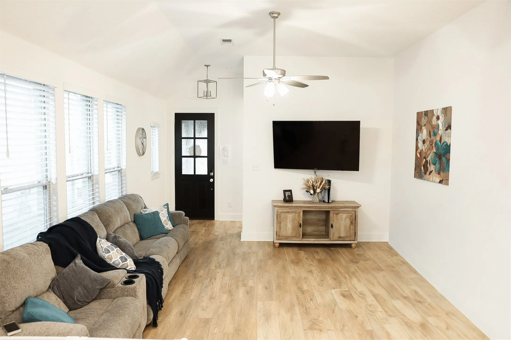 Spacious living area featuring wood-finish flooring, a vaulted ceiling, and multiple windows with blinds