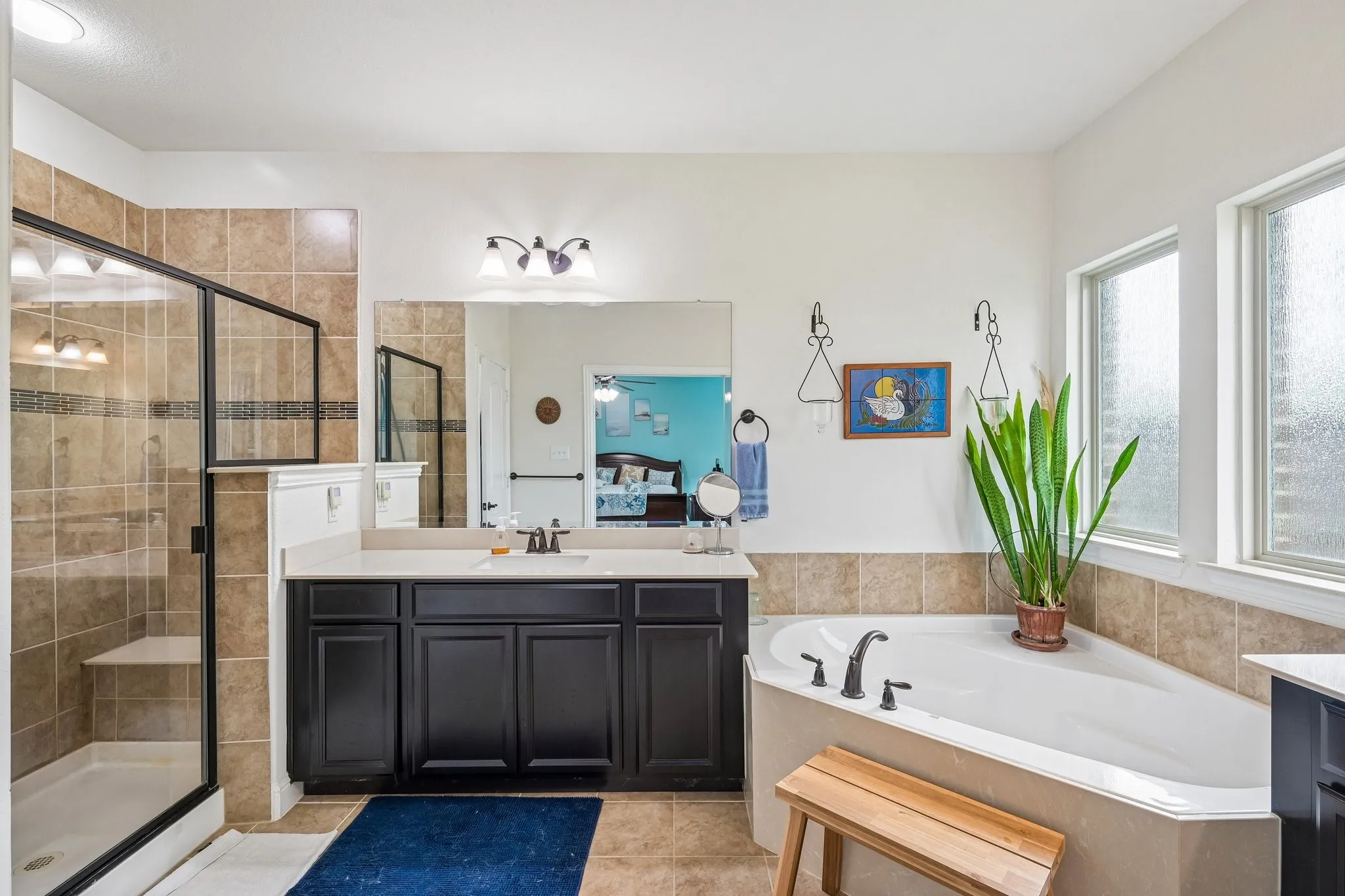 Spacious bathroom featuring a built-in soaking tub, a separate glass-enclosed shower with a built-in bench, a vanity with a dark cabinet base and light countertop, and multiple windows
