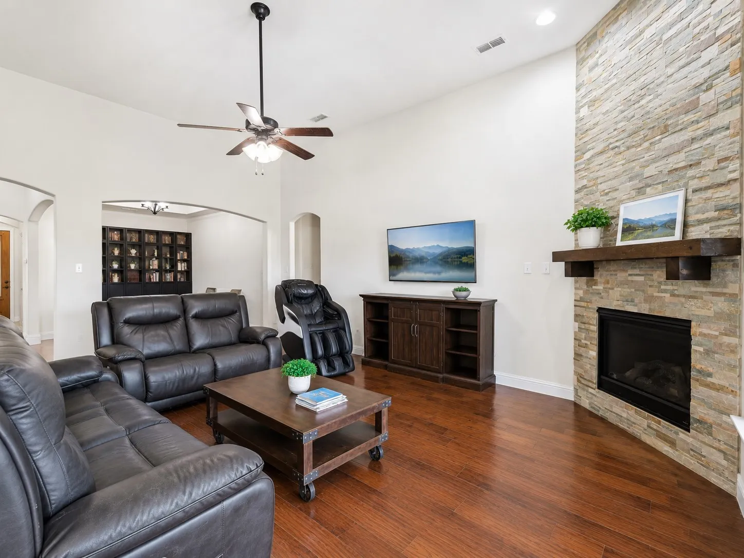Living area featuring wood-finish flooring, a stacked stone fireplace with a wood mantel, vaulted ceilings, and recessed lighting