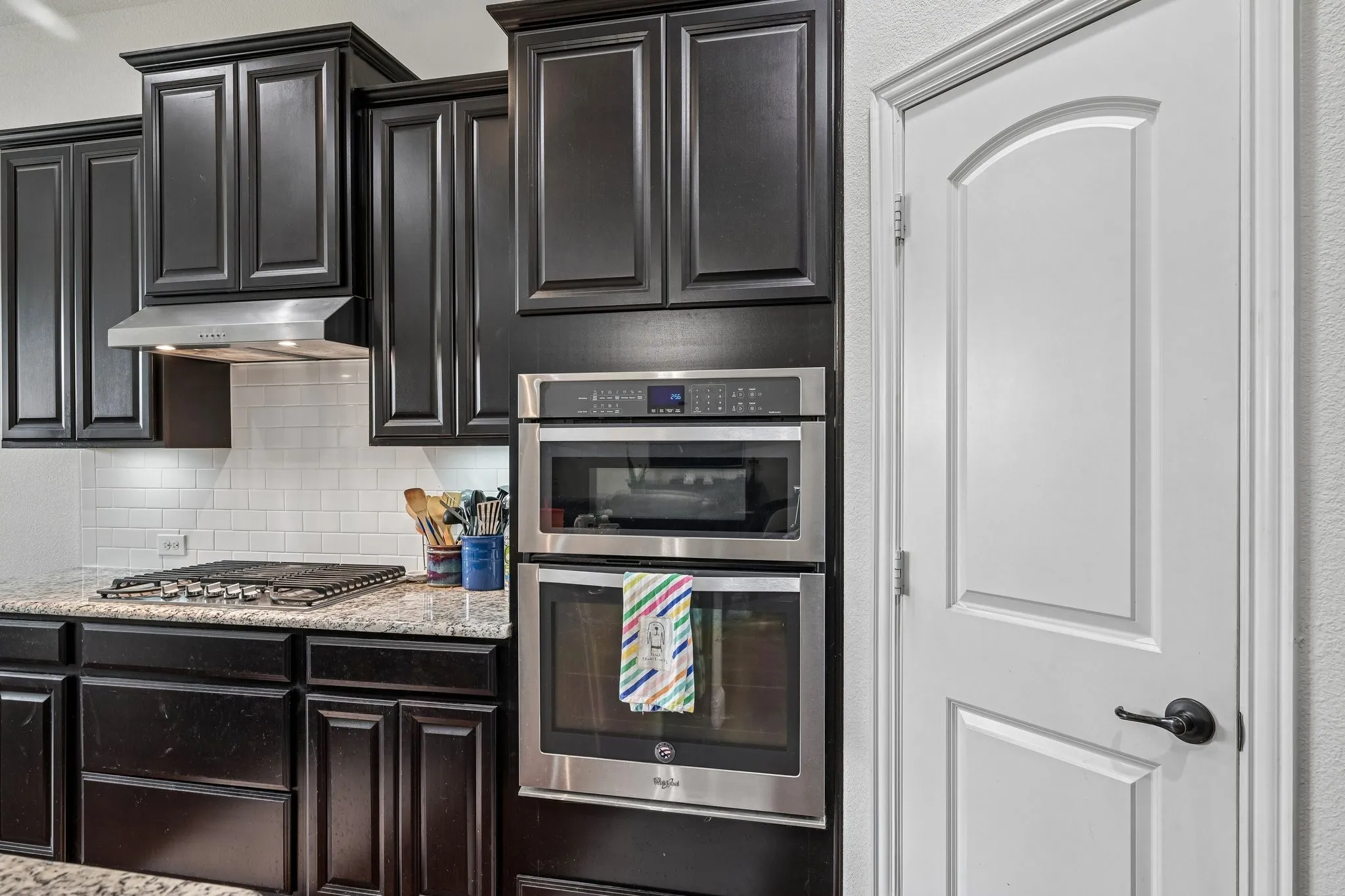 Kitchen featuring dark wood cabinetry, granite-finish countertops, subway tile backsplash, and stainless steel appliances including a built-in oven and microwave