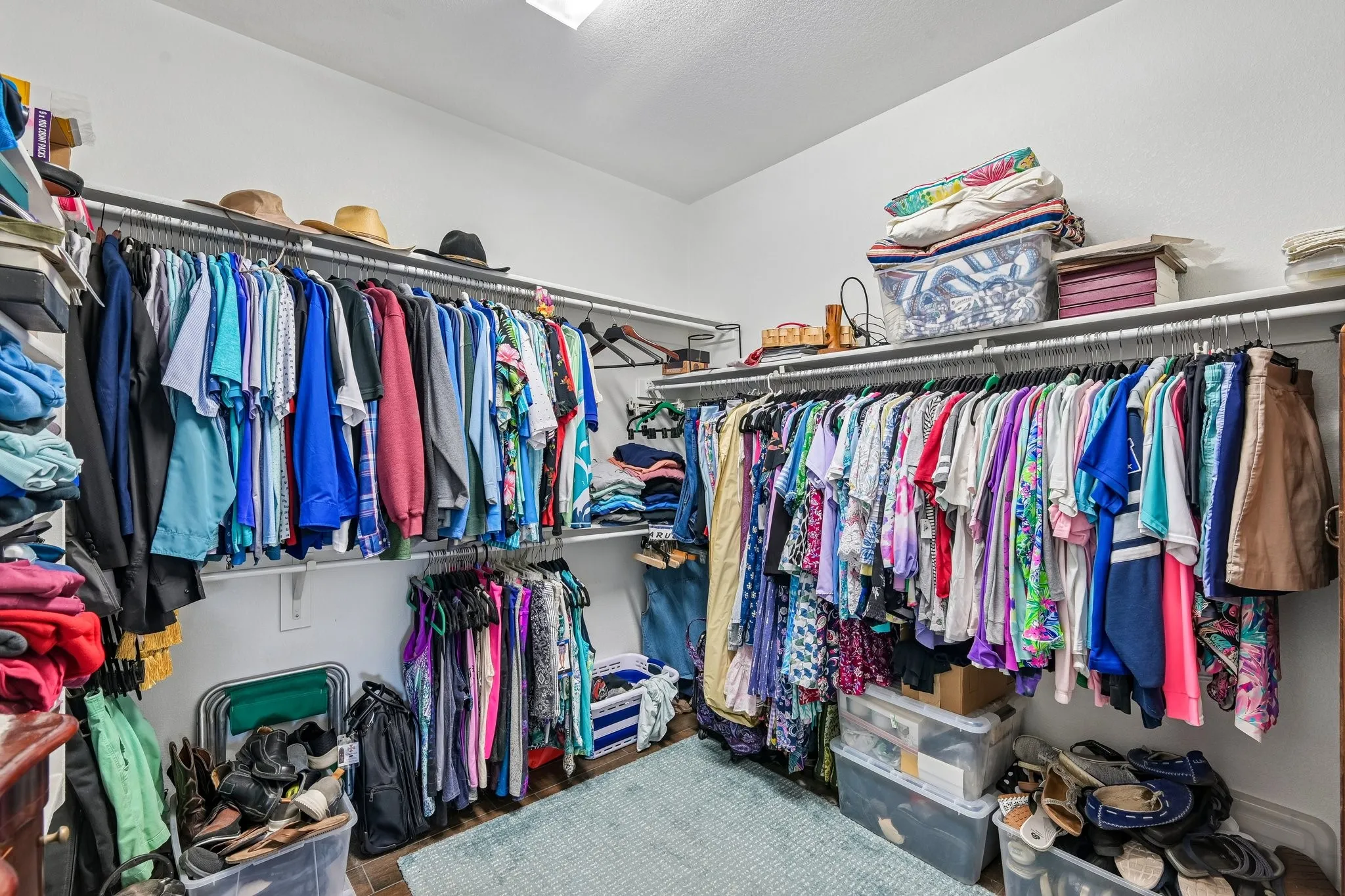 Spacious walk-in closet featuring white walls, wood-finish flooring, and multiple levels of shelving and hanging rods