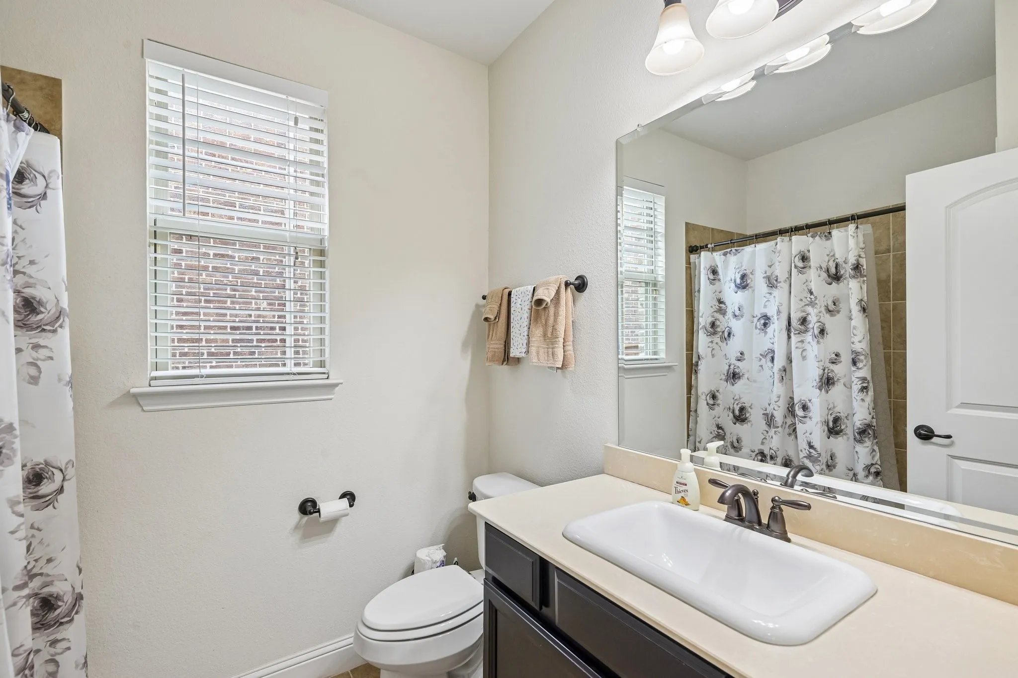 Full bathroom featuring a single vanity with a rectangular sink, light-toned countertop, and dark wood-finish cabinetry