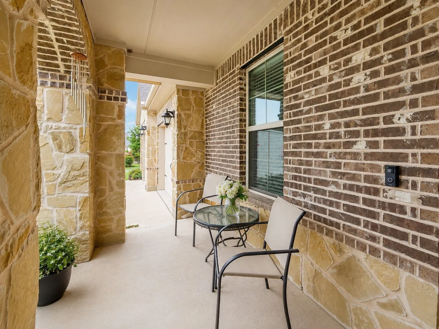 Covered front porch featuring a concrete surface, stone veneer columns, and a brick exterior wall