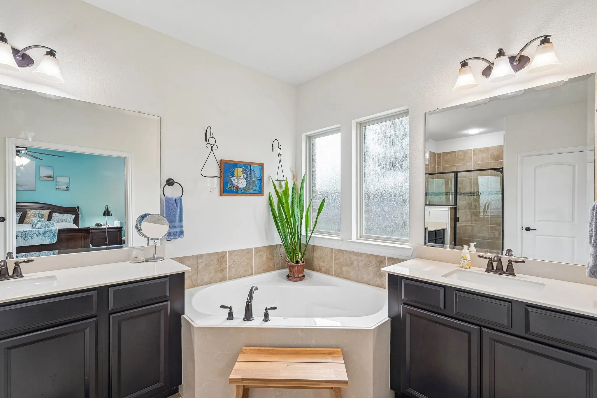 Soaking tub with a tiled surround, framed by two frosted windows, and flanked by dual vanities