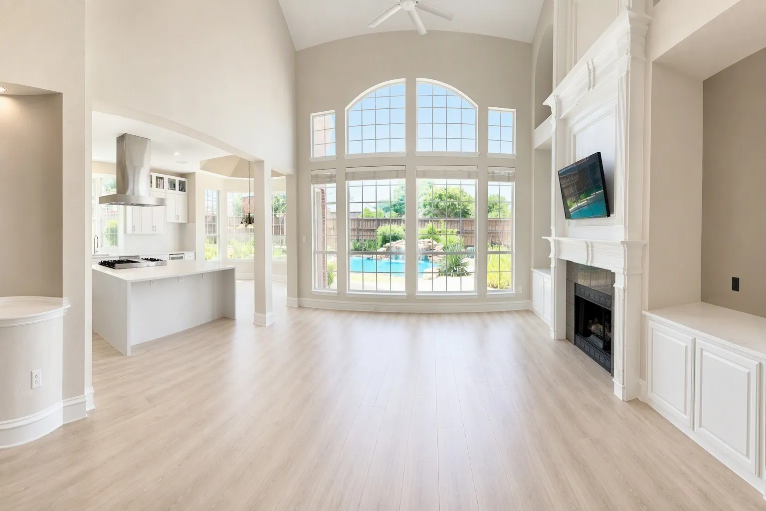 Spacious living area featuring light wood-finish flooring, a grand fireplace with ornate white surround, and built-in cabinetry