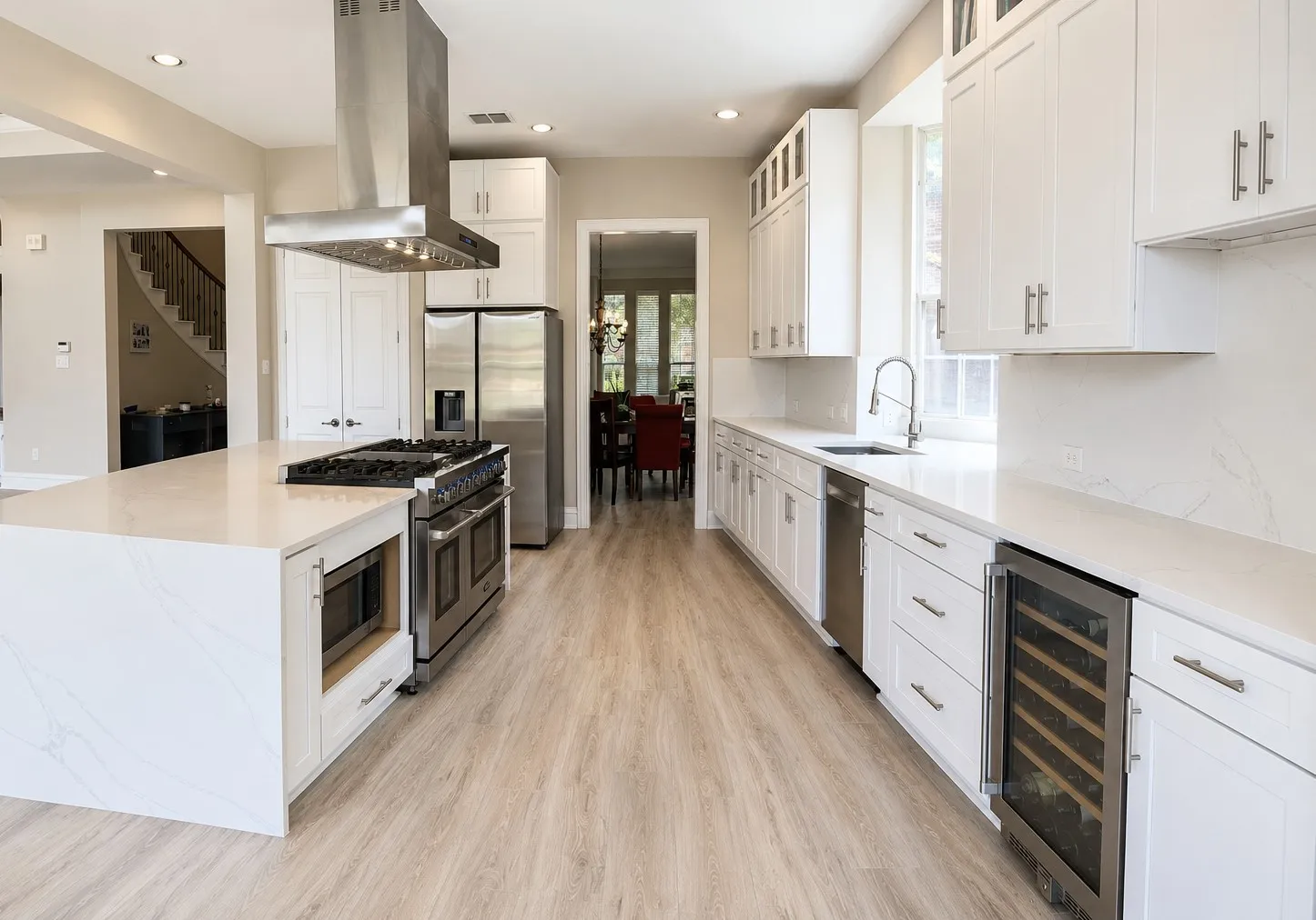 Gourmet kitchen featuring a substantial island with integrated microwave, stainless steel range with overhead vent hood, ample white cabinetry, integrated wine cooler, and light wood-finish flooring
