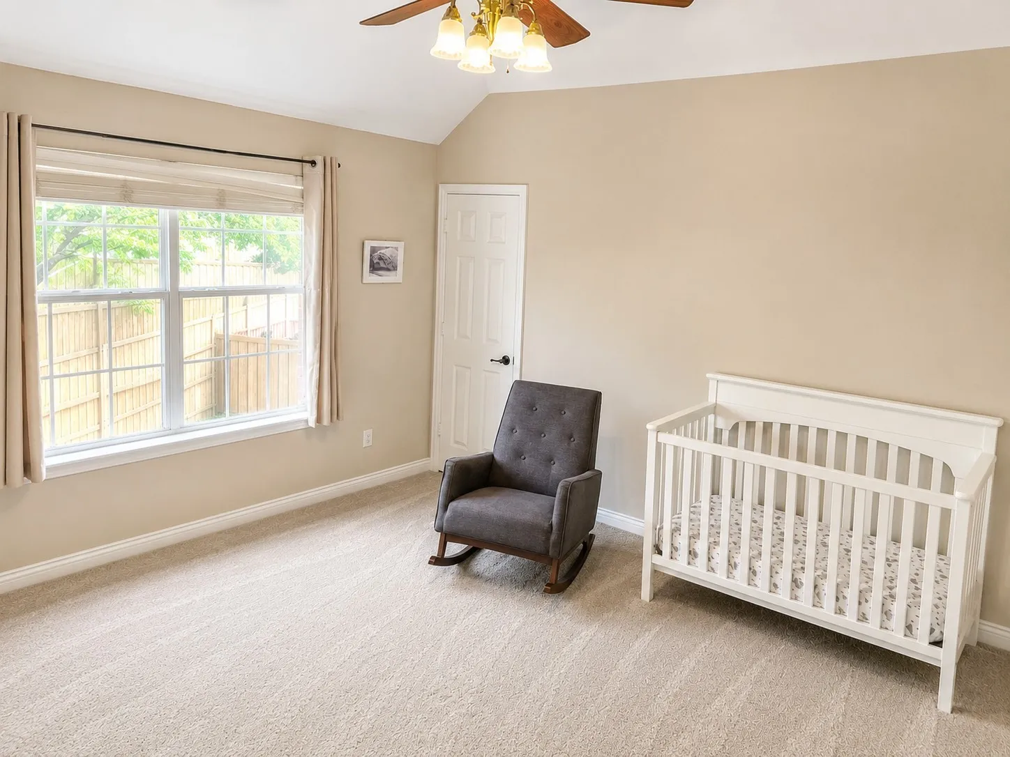 Carpeted room featuring a double-hung window, vaulted ceiling, ceiling fan with light fixture, and a solid core door