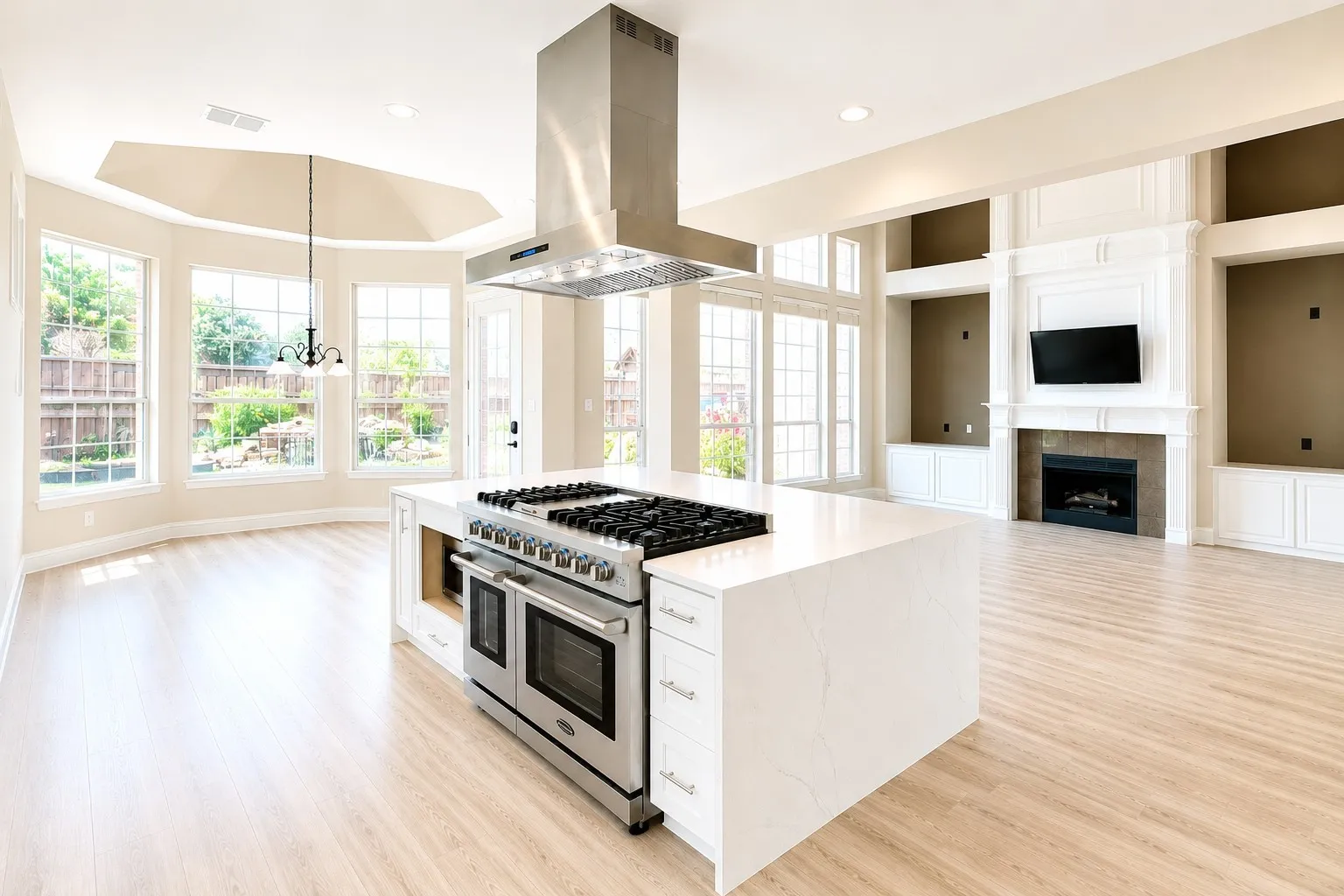Open-concept living space with light wood-finish flooring, a contemporary kitchen island featuring a stainless steel range and hood, and an integrated fireplace with built-in cabinetry and shelving