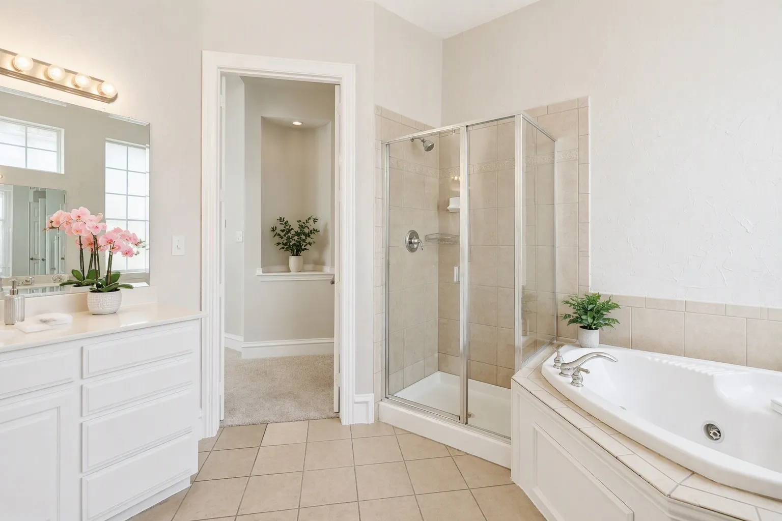 Bathroom featuring a corner soaking tub, a separate glass-enclosed shower, a vanity with ample counter space, a large mirror, and tiled flooring