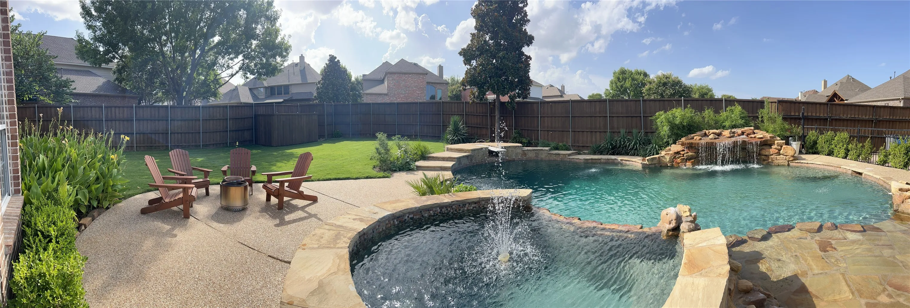 Expansive backyard featuring a large swimming pool with a rock waterfall, an integrated spa with a water feature, natural stone coping, and a surrounding aggregate patio