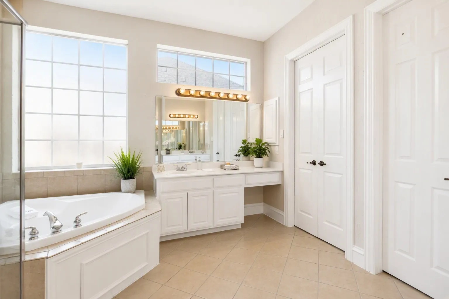 Corner soaking tub with tile surround, dual vanity with undermount sinks, and separate frosted windows